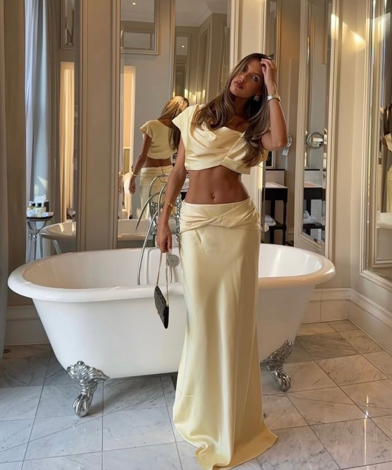Woman in a beige outfit standing in a bathroom with a freestanding bathtub.