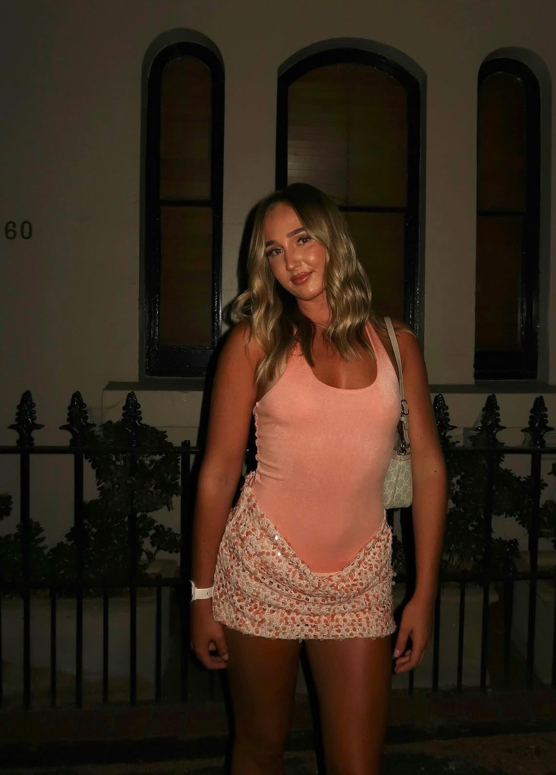 Woman in a pink top and floral skirt standing in front of a building with arched windows. - @emilyferriis