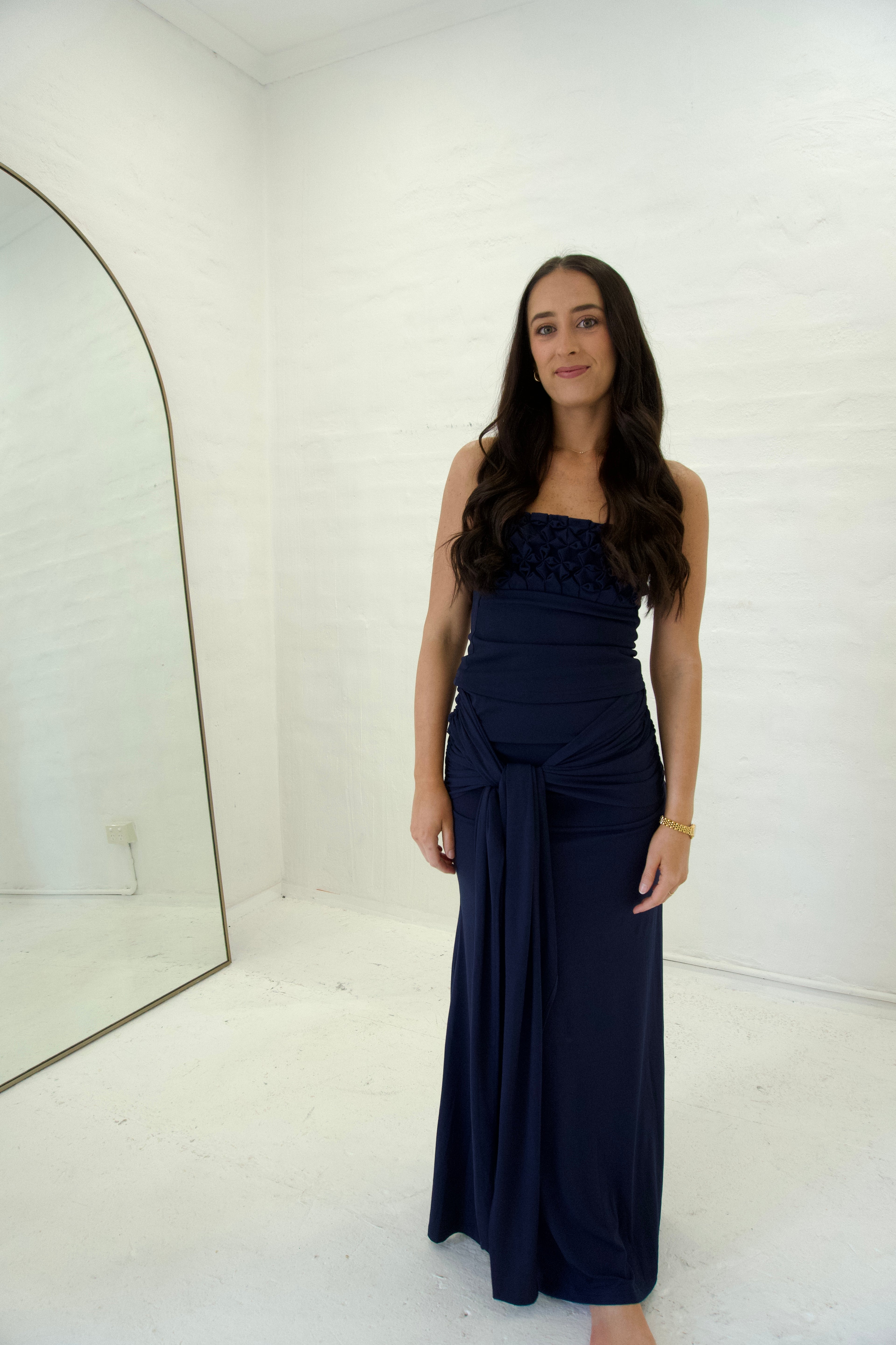 Woman wearing a navy blue strapless gown in a white room.