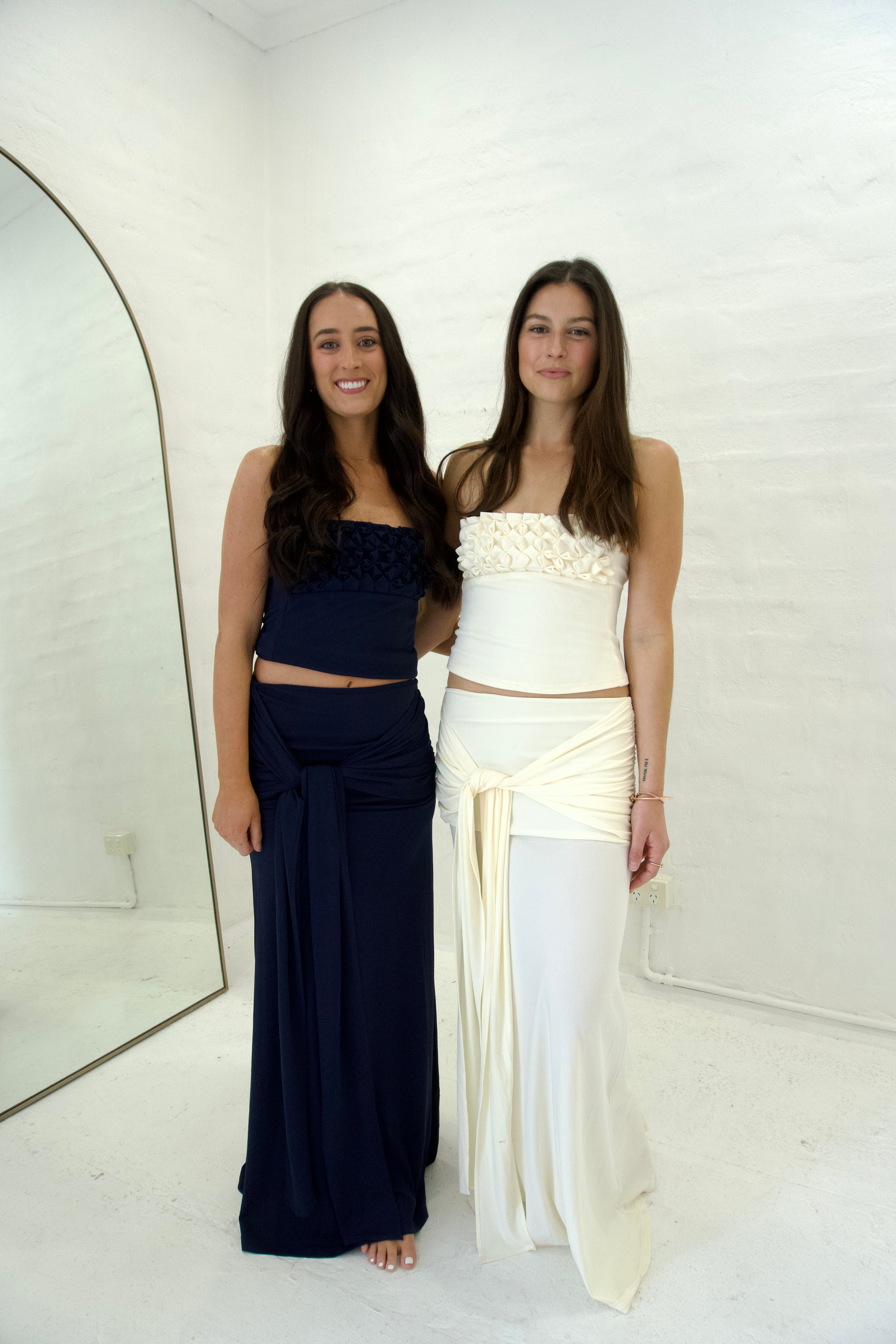 Two women in formal sets standing against a white background