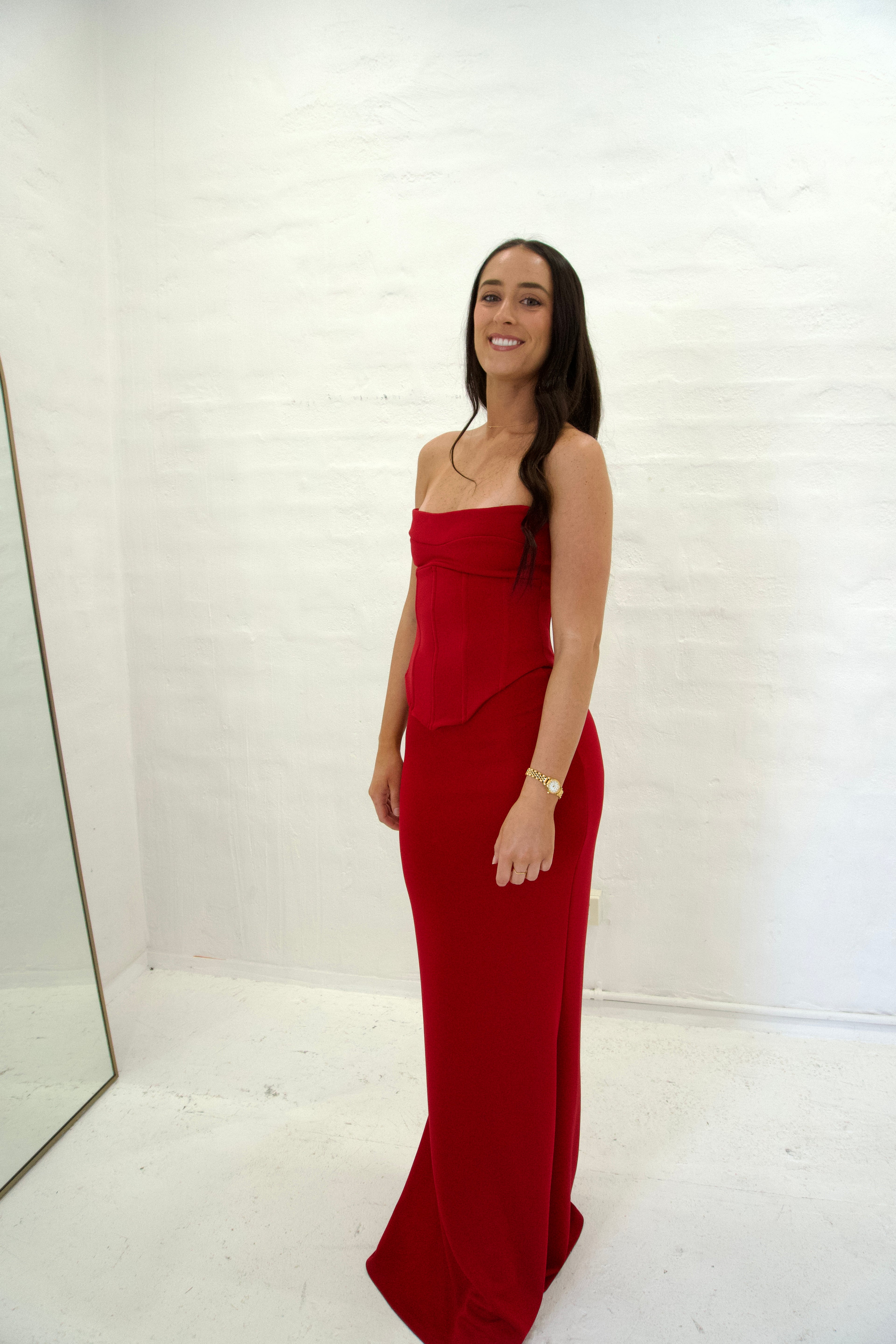 Woman wearing a red strapless gown standing against a white wall.