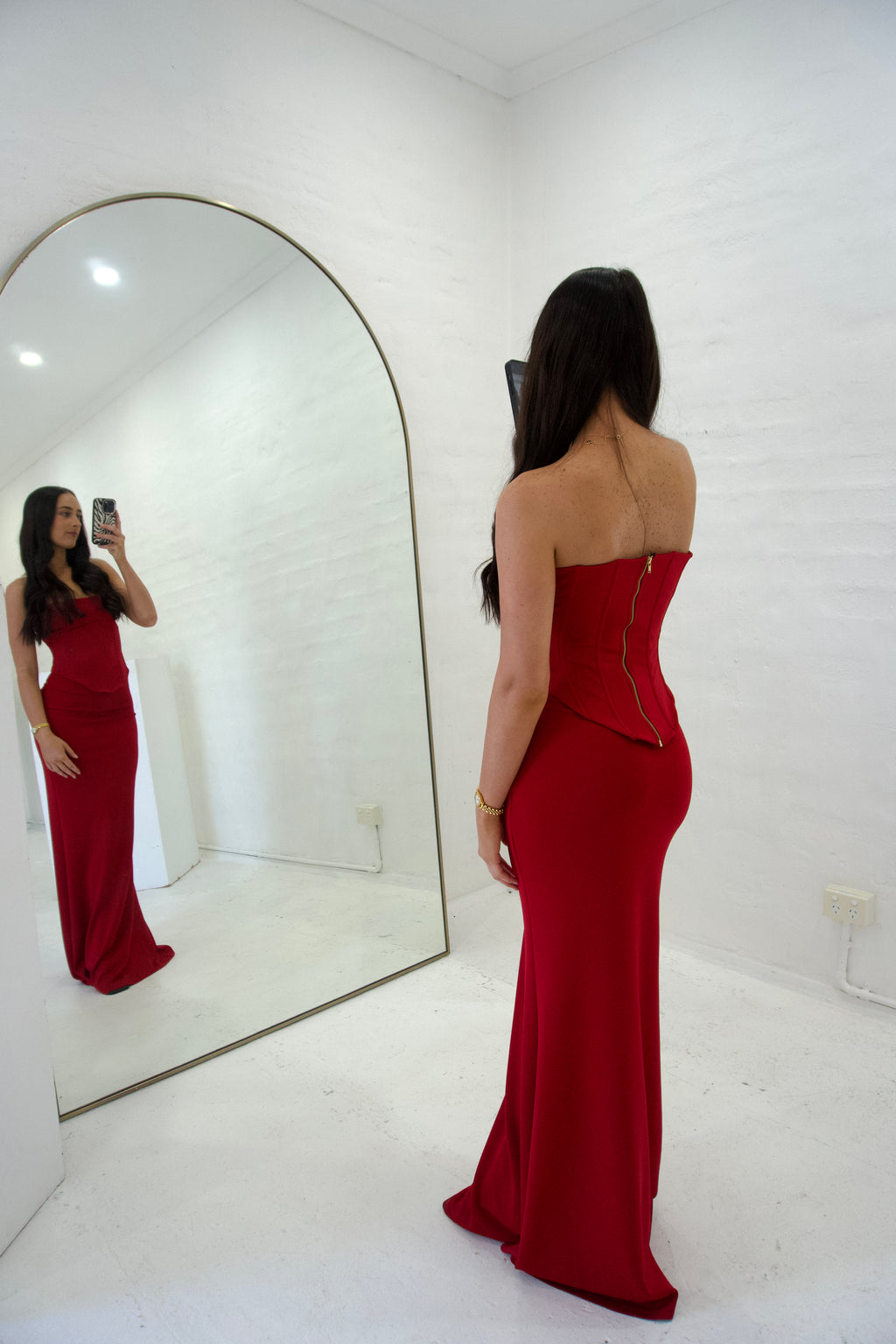 Woman in a red strapless gown standing in front of a mirror.
