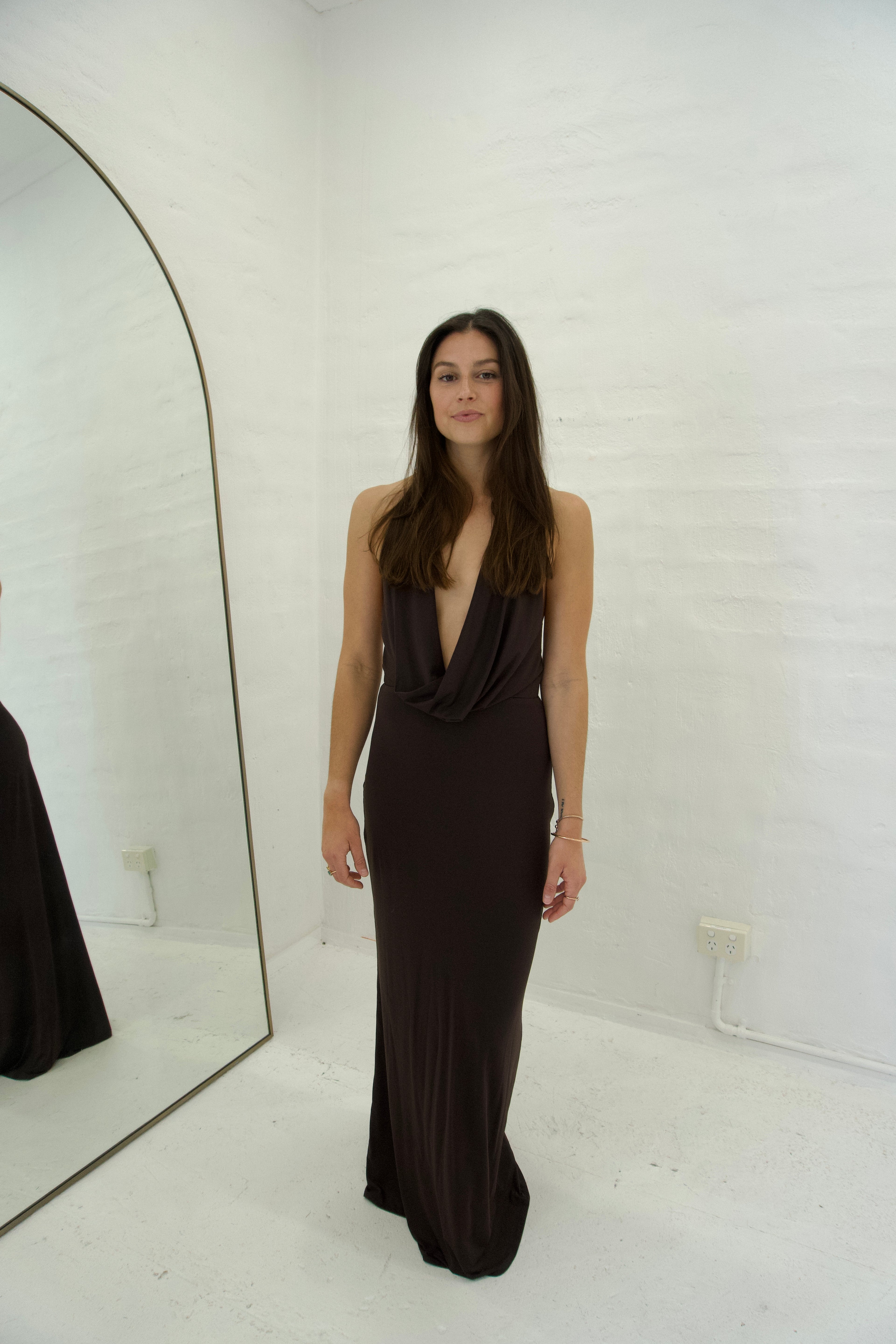 Woman wearing a black evening gown in a minimal white room.