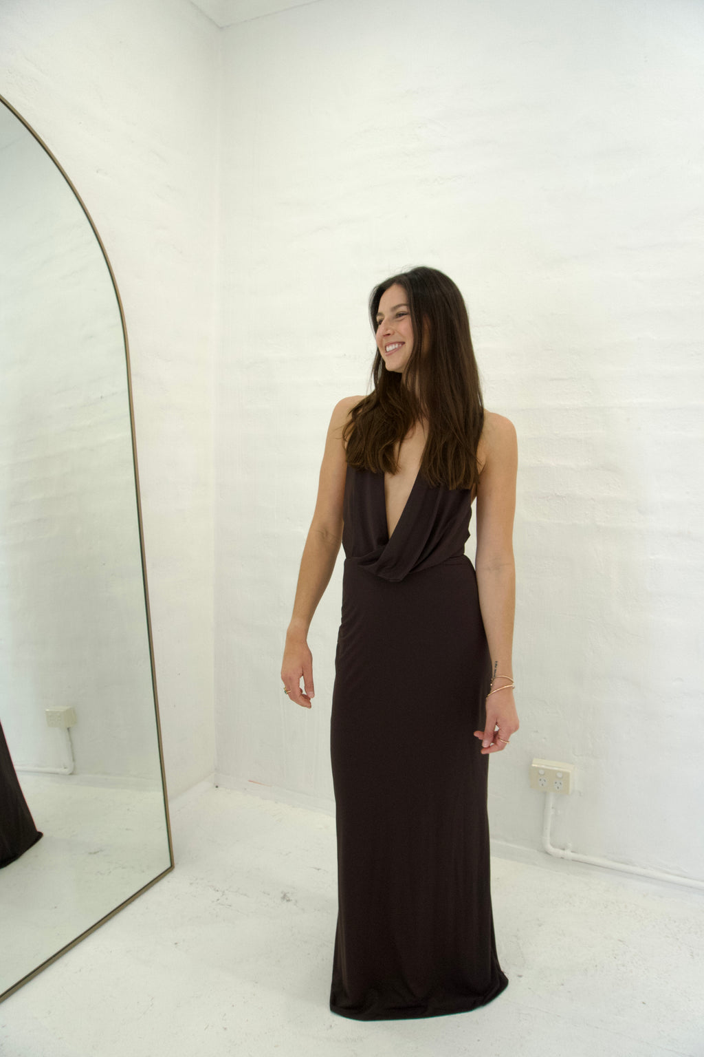 Woman in a black evening gown standing in a room with a mirror.