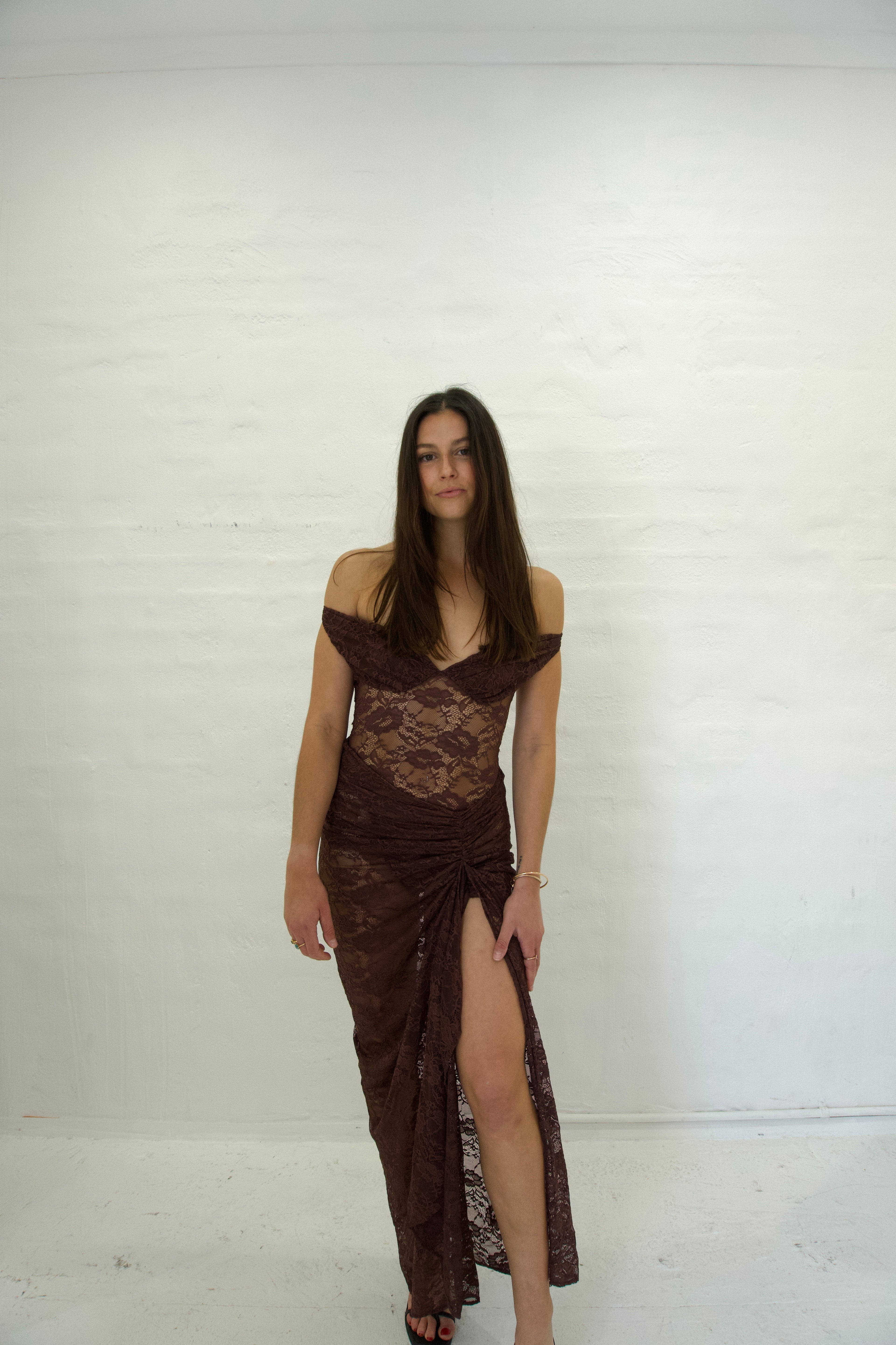 Woman wearing a brown lace dress with a slit on a white background