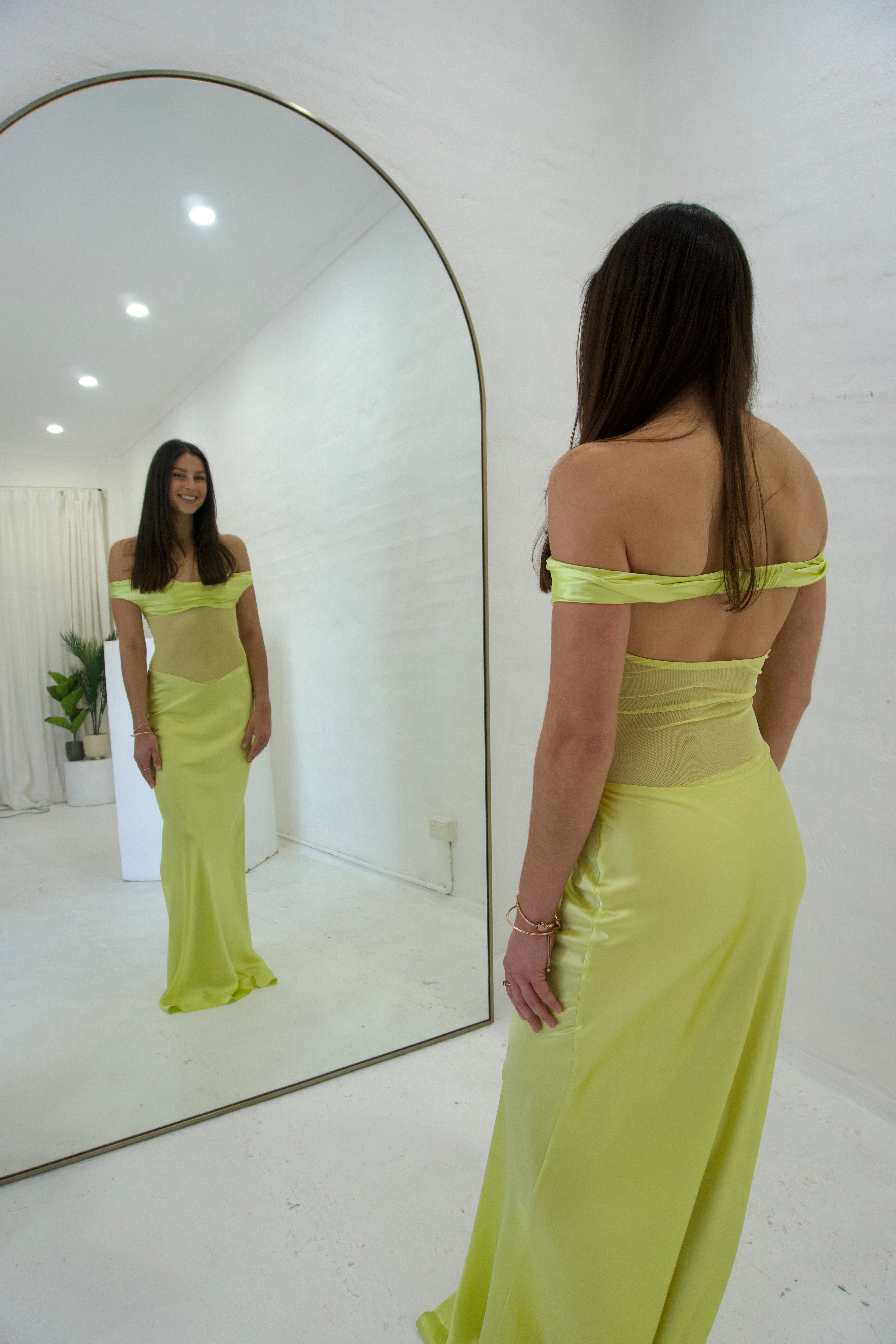 Woman in a bright yellow dress standing in front of a mirror in a minimalistic room.