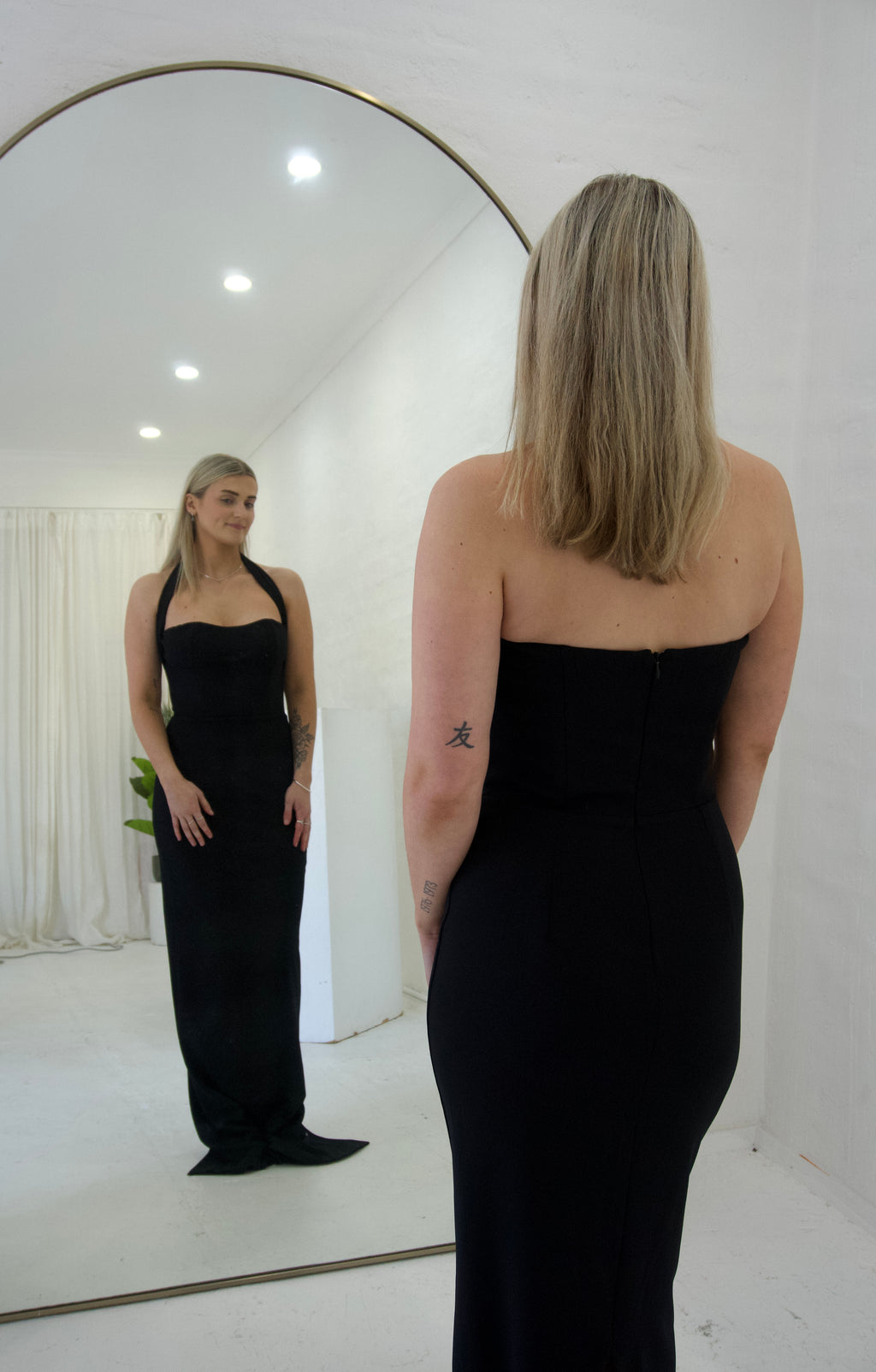 Woman wearing a black strapless dress standing in front of a mirror.