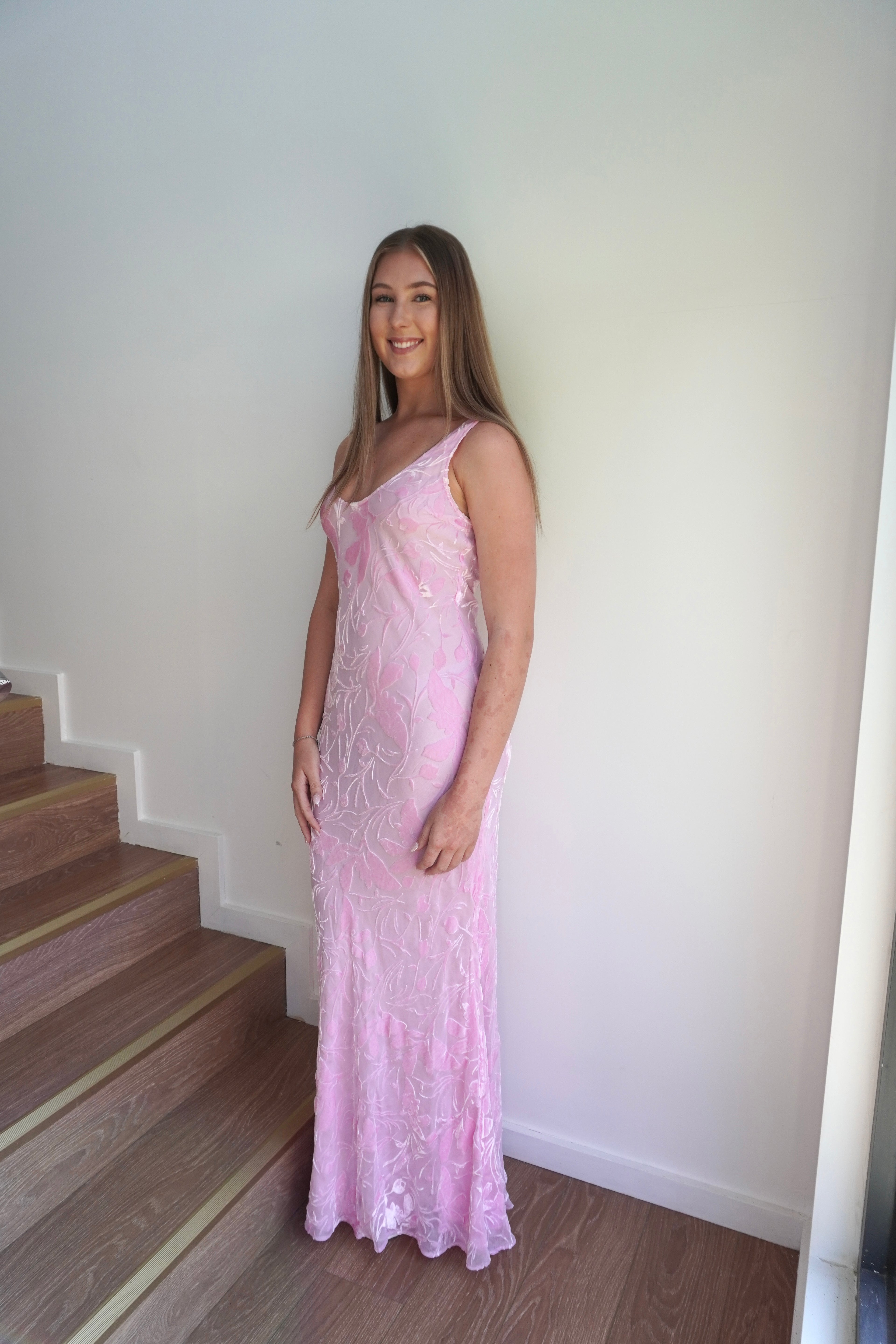 Woman in a pink lace dress standing on a staircase.
