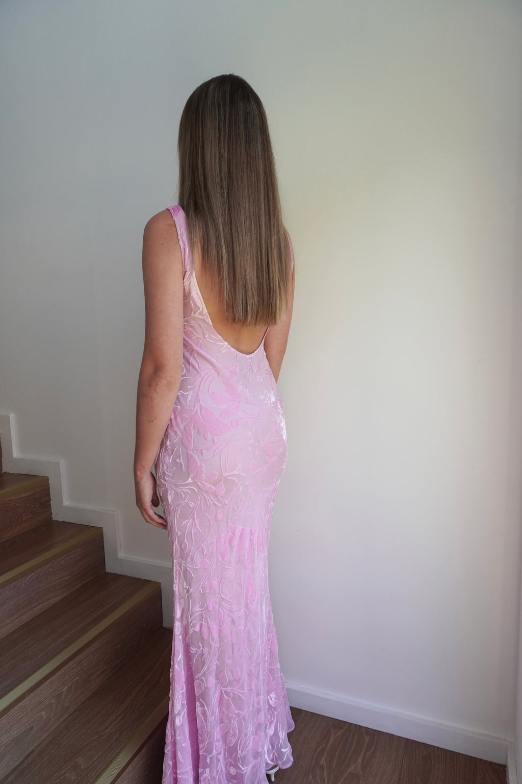 Woman in a pink dress standing on a staircase against a white wall