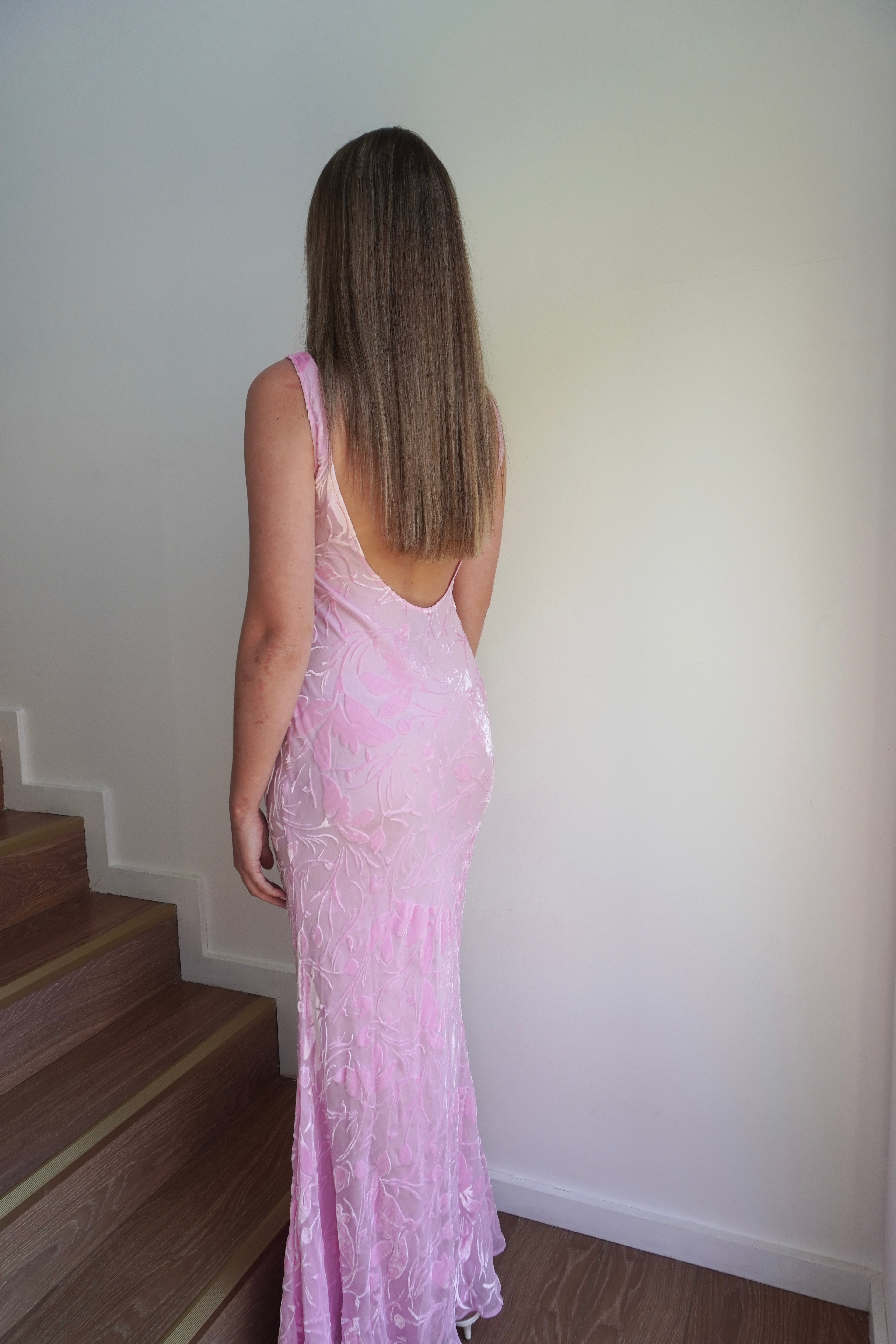 Woman in a pink dress standing on a staircase against a white wall