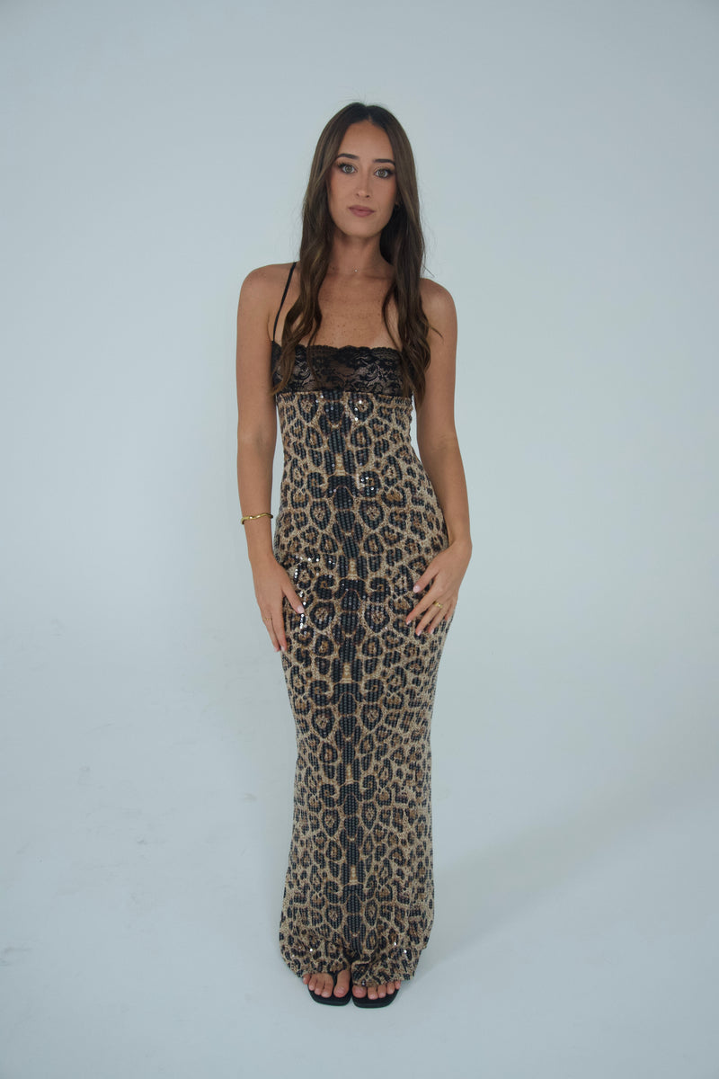 Woman wearing a floor-length leopard print sequin gown with thin straps and black lace detailing across the neckline, photographed against a light grey studio background. - @sarahmadden