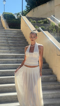 Woman in a white dress standing on outdoor steps with a clear sky