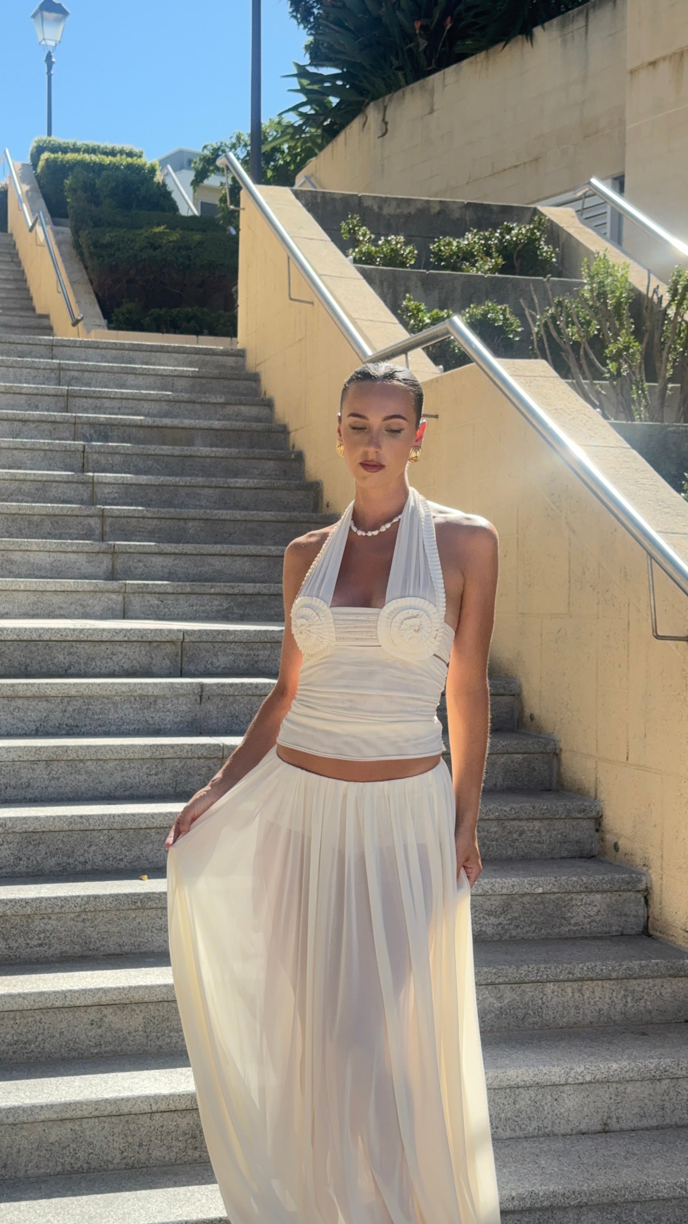 Woman in a white dress standing on outdoor steps with a clear sky