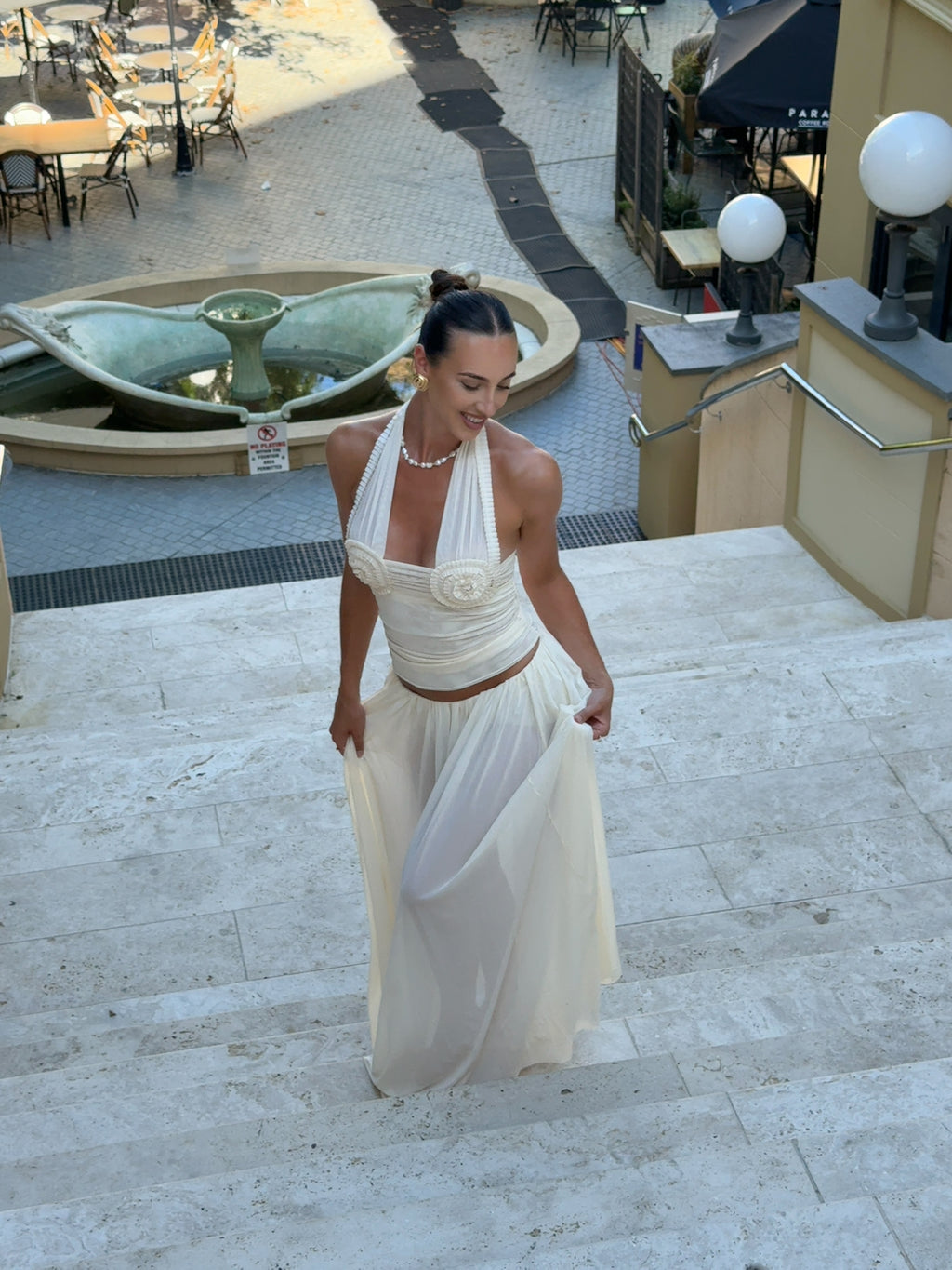Woman in a white dress standing on steps with a fountain in the background