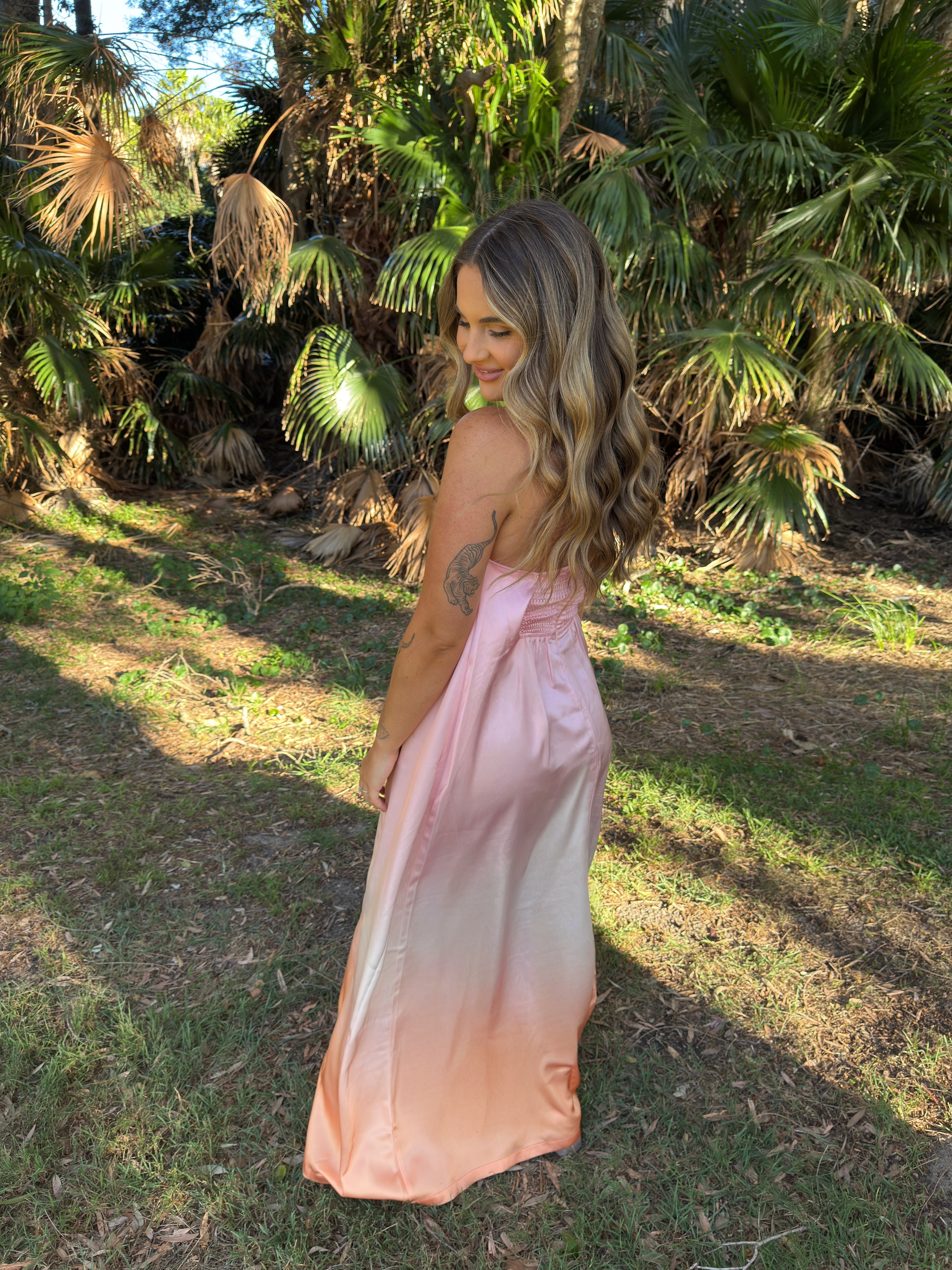 Woman in a pink dress standing in a natural setting with greenery