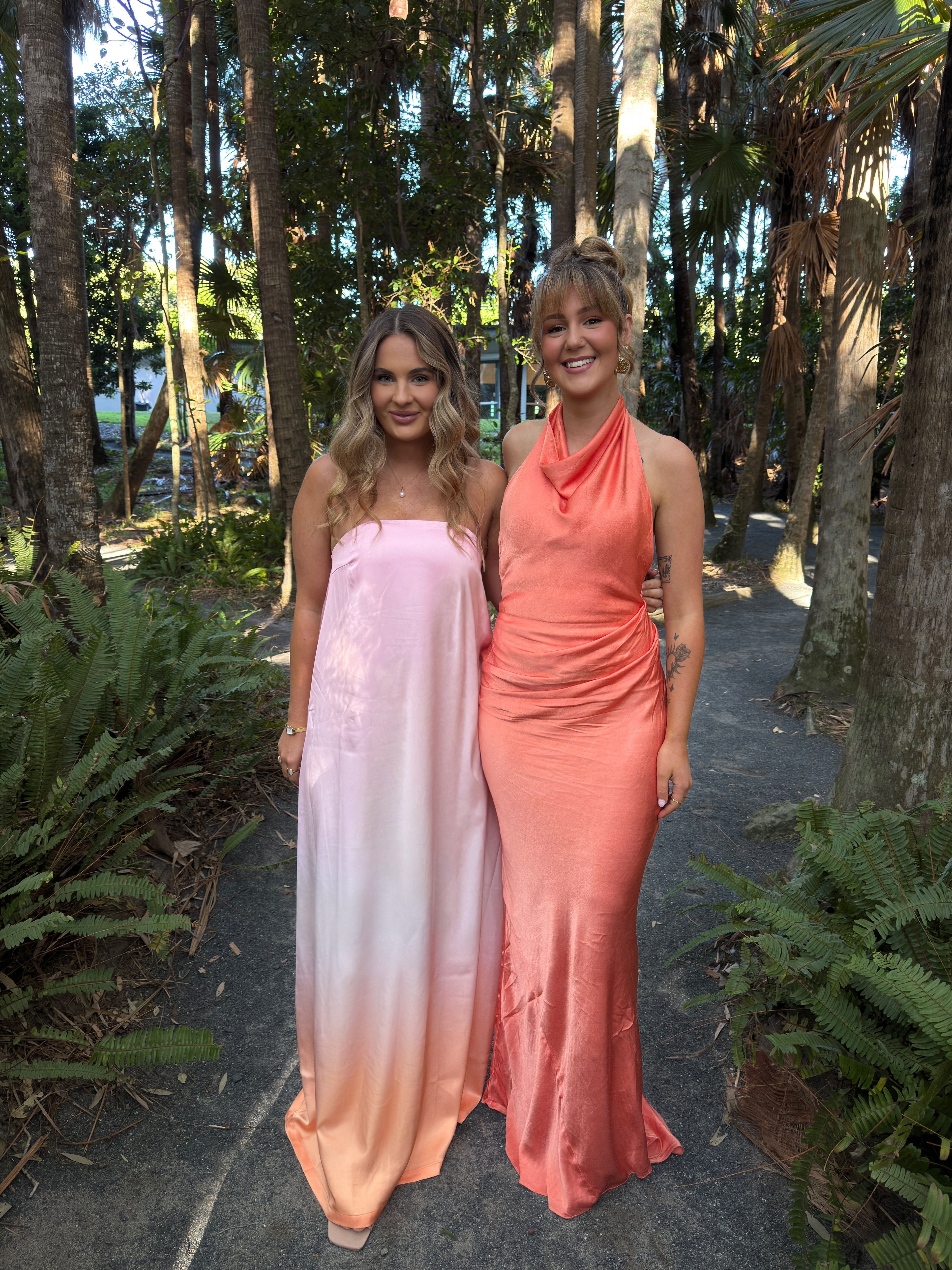 Two women in pink dresses standing in a forested area.