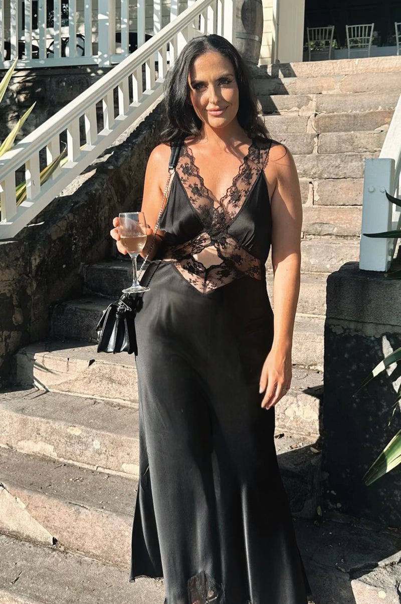 Girl in black maxi dress standing infront of stairs holding a wine glass. - @gabmoore
