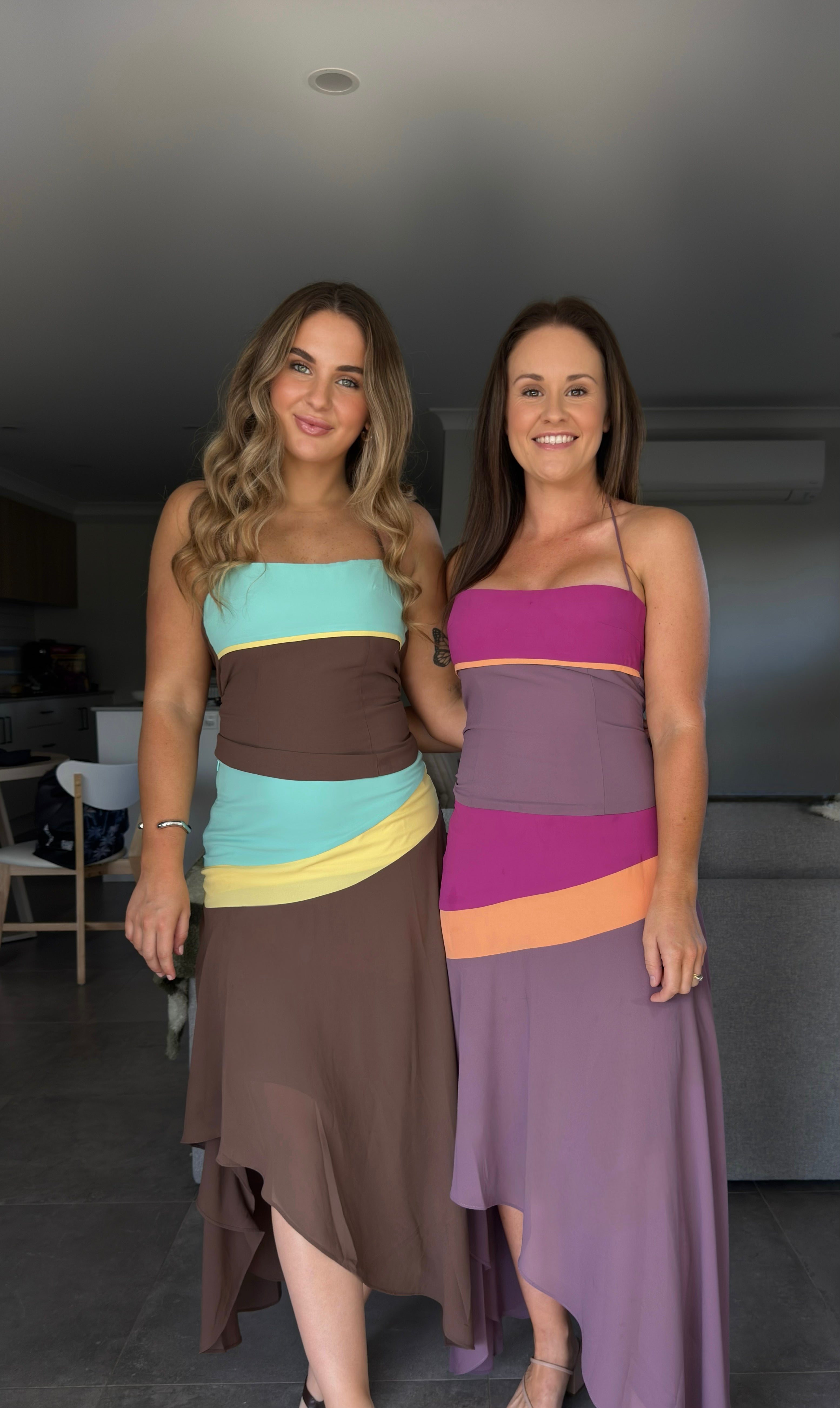 Two women wearing colorful dress outfits standing indoors.