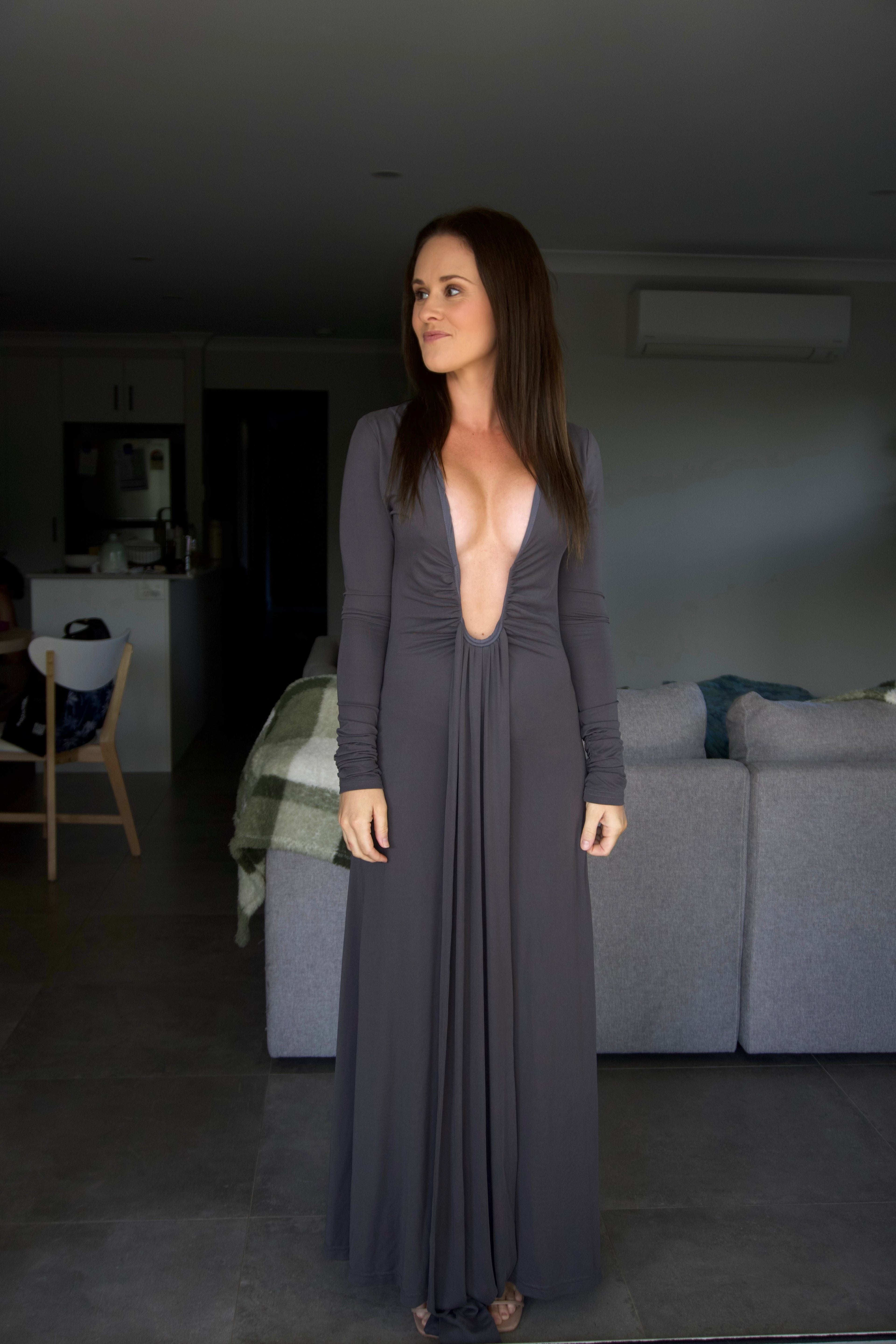 Woman in a long dark gray dress standing in a dimly lit room.