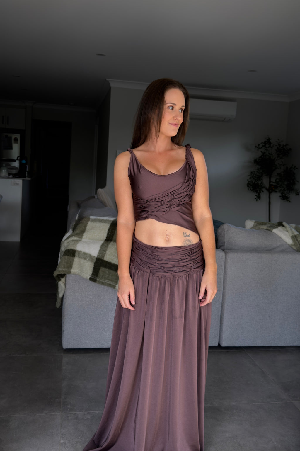 Woman wearing a long brown dress standing in a room with gray walls and furniture.