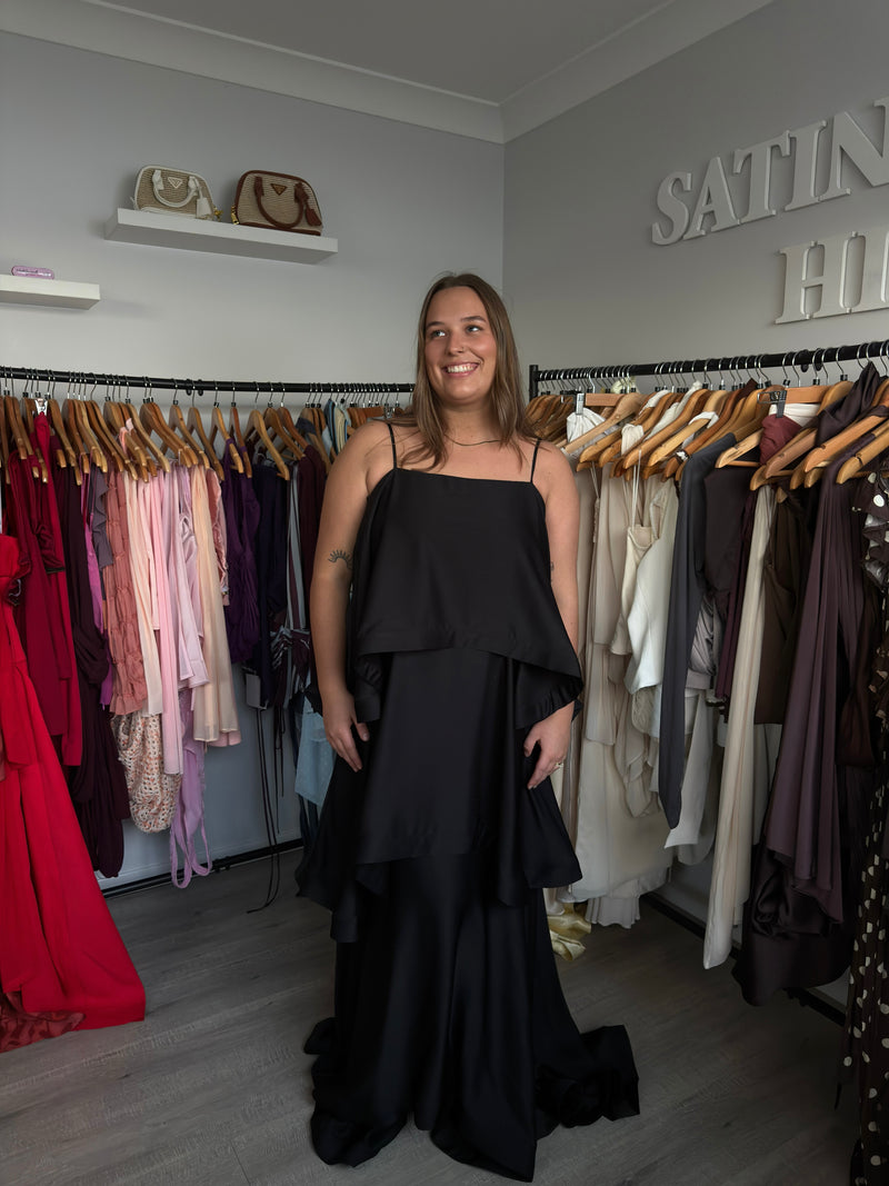 Woman in a black evening gown standing in a clothing store with racks of dresses. - @chelseabowditch