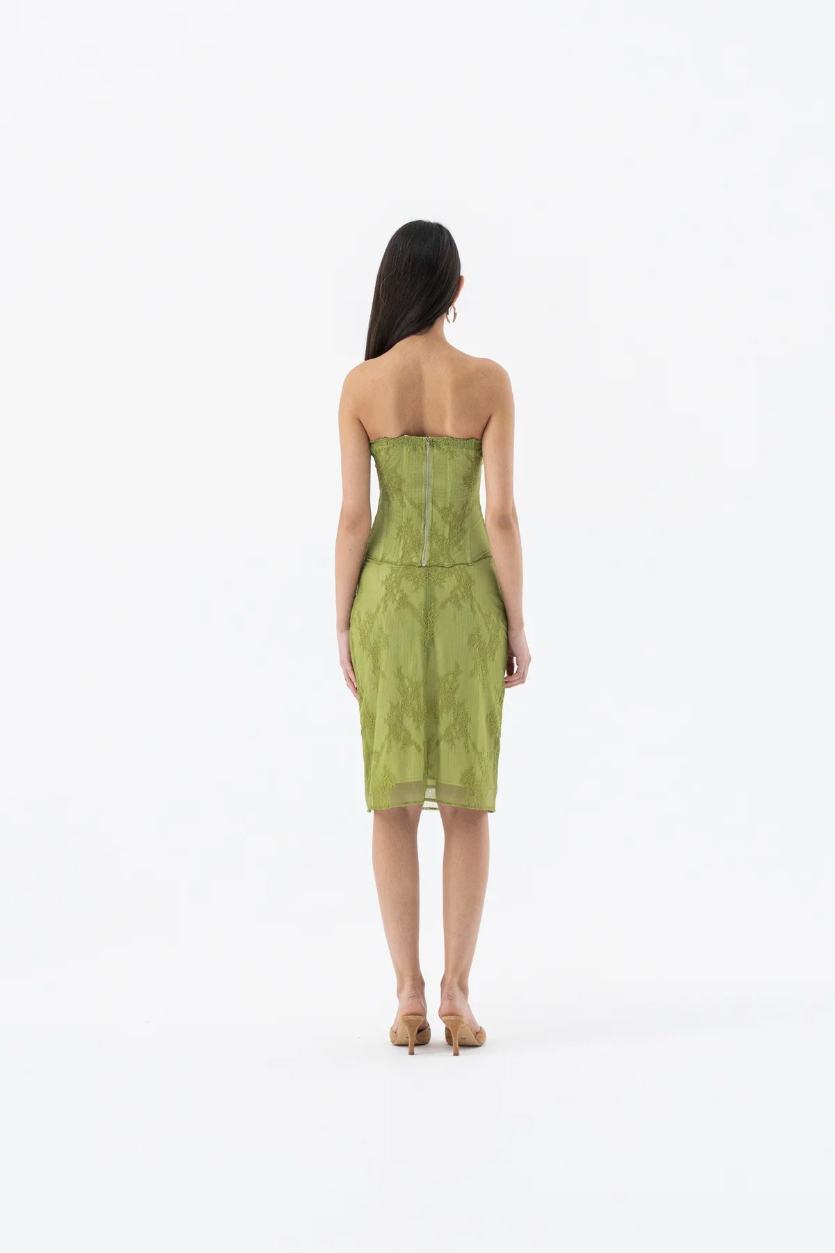 A woman viewed from behind wearing a strapless olive green midi dress with a textured pattern, standing against a plain white studio background.