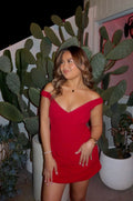 A woman posing in a red off-the-shoulder mini dress, standing in front of large potted prickly pear cacti at night.