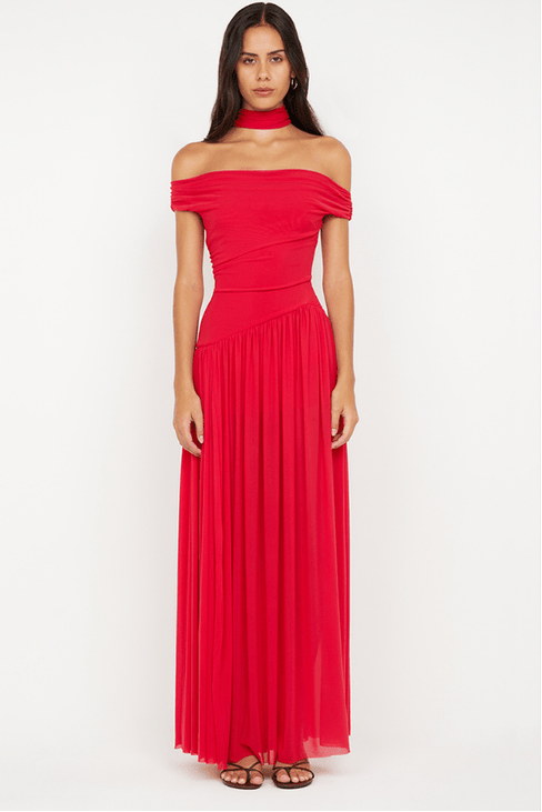 A woman modeling a bright red off-the-shoulder maxi dress with a pleated skirt, paired with a matching red choker and brown strappy sandals, against a plain white studio background.