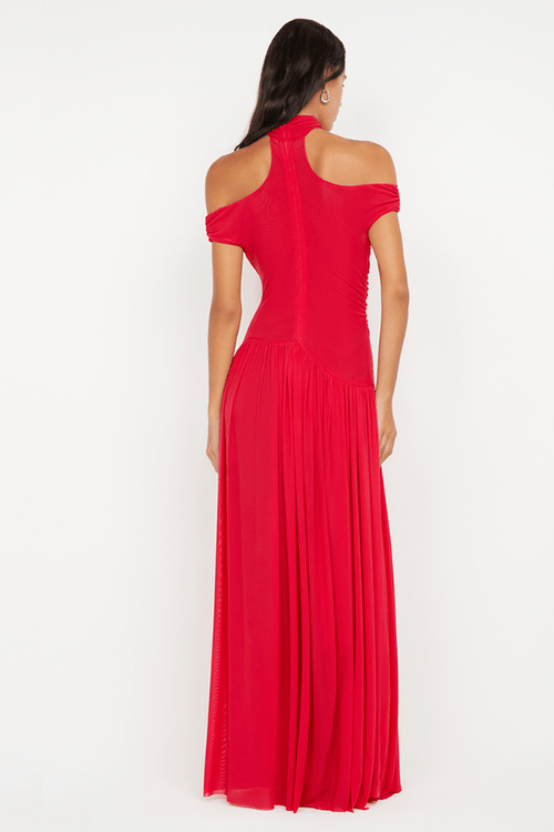 A woman modeling a bright red off-the-shoulder maxi dress from the back, featuring a structured bodice and a flowing pleated skirt, set against a plain white studio background.
