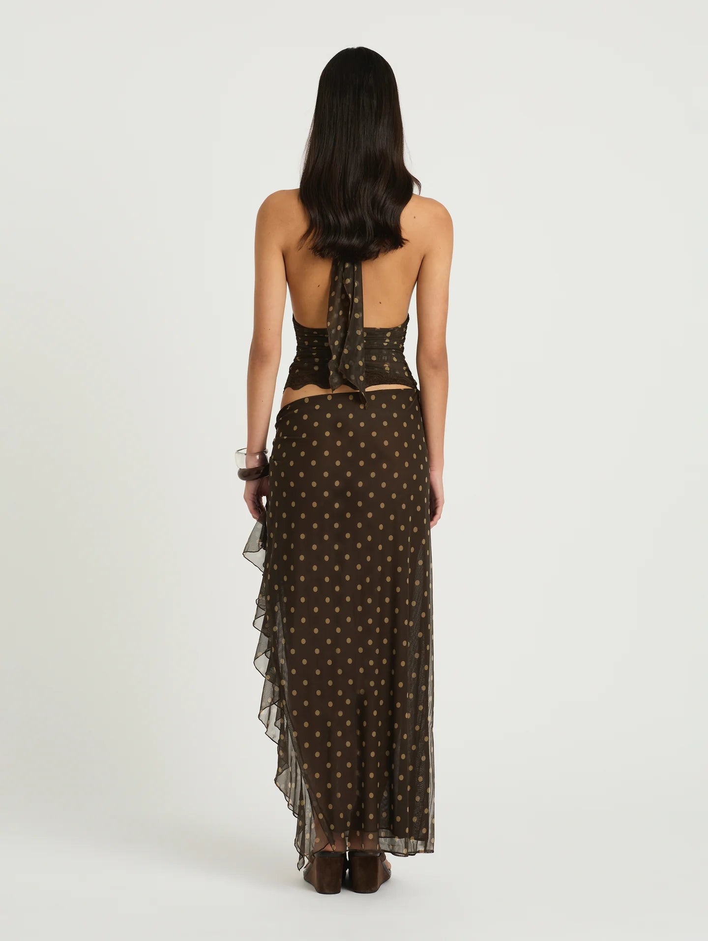 Woman wearing a brown polka dot dress with sheer overlay on a white background