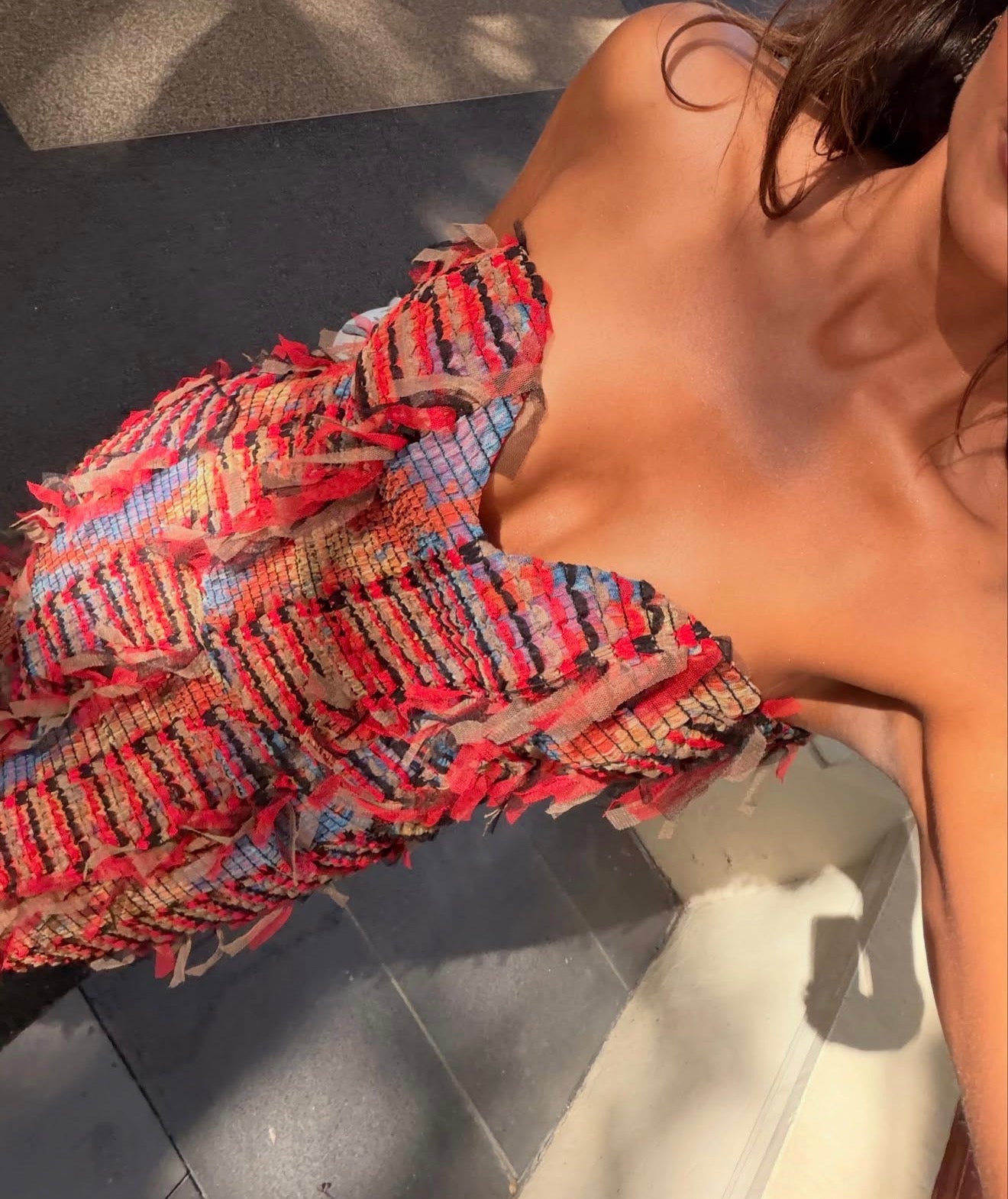 Picture of a strapless red dress on a girl standing on pavement.