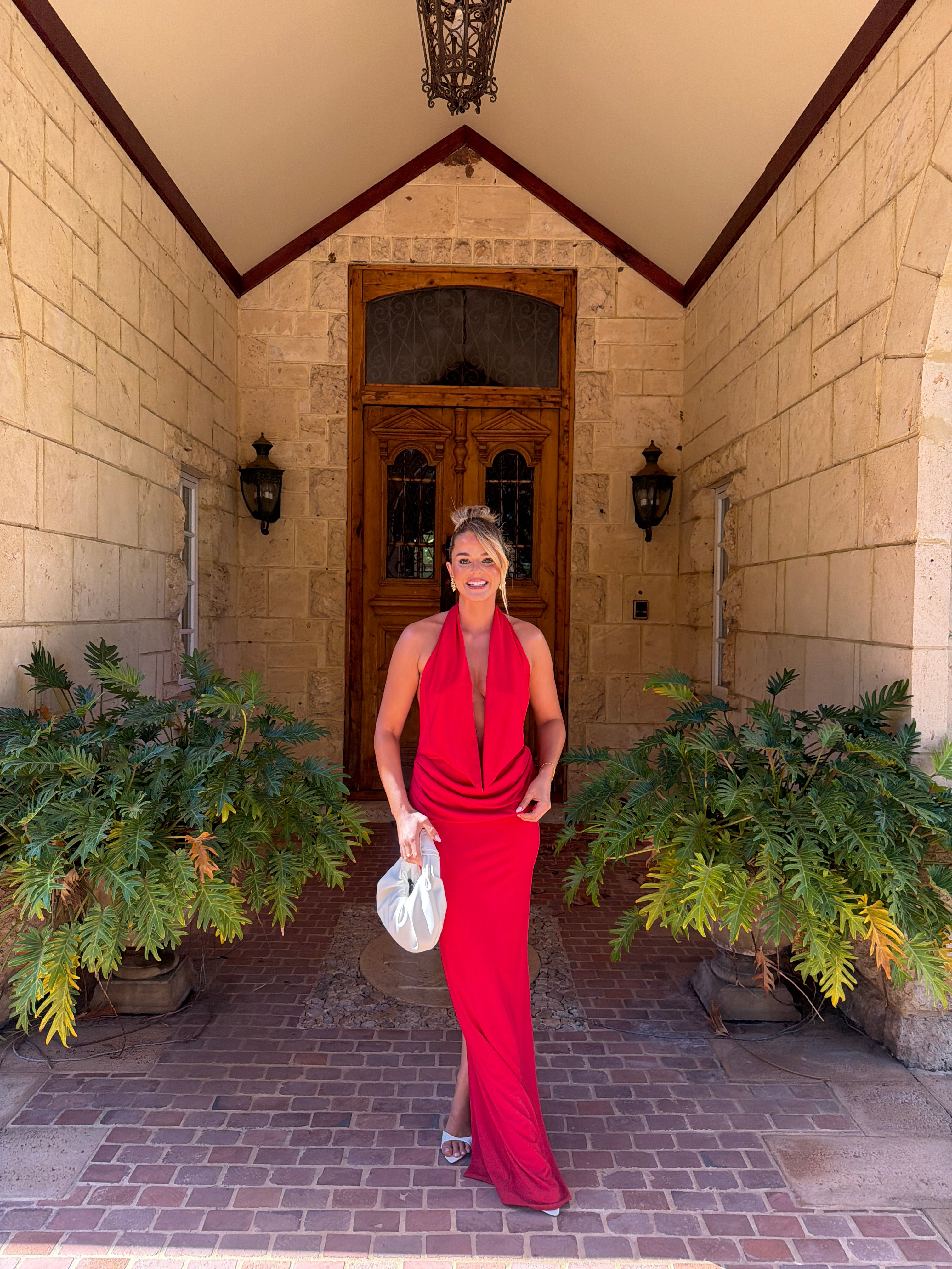 Person in a red dress standing in front of a decorative door with plants around. - @elizakohler
