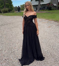 Woman in a black off-shoulder evening gown standing on a gravel path with greenery in the background. - @kaitlinknightt
