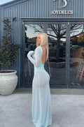 Girl standing in front of a door wearing a blue backless sheer dress with long sleeves.