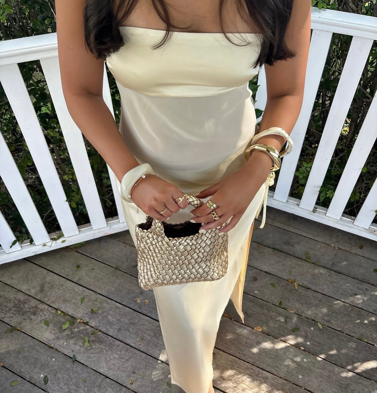 Woman holding a beaded handbag on a wooden deck with white railing.