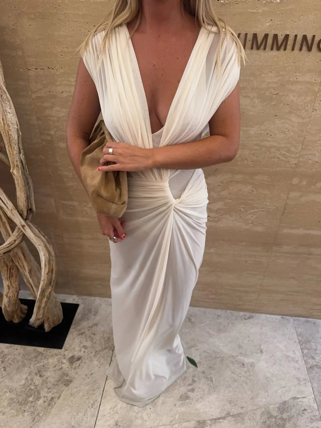 Woman in a white dress standing against a beige wall.