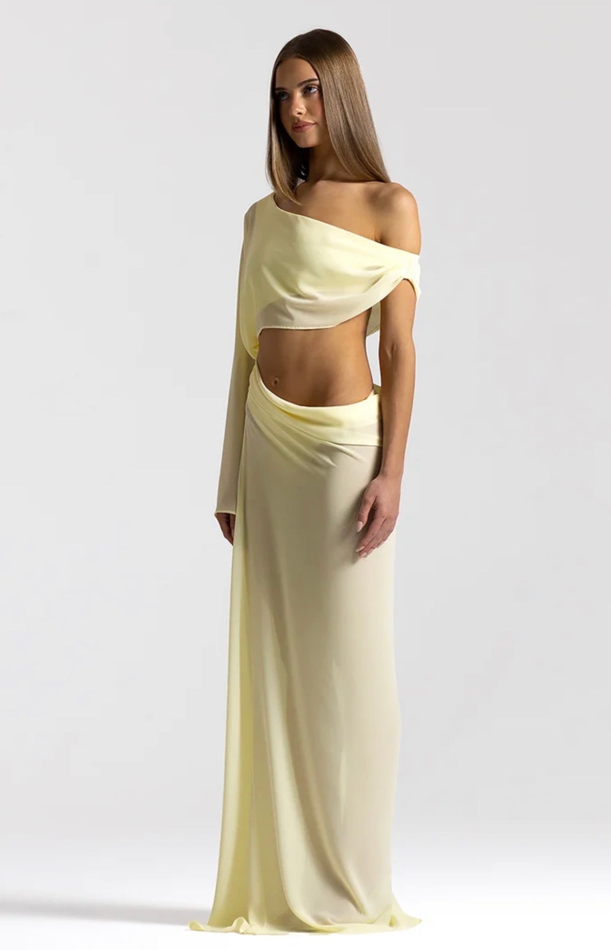 Girl in front of a white backdrop with yellow cutout dress that falls off the shoulder