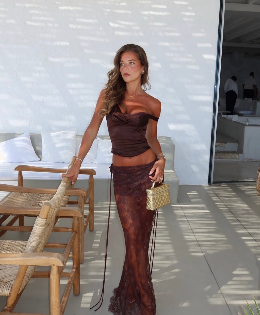 Girl wearing a brown lace set, holding a handbag in front of a white background.