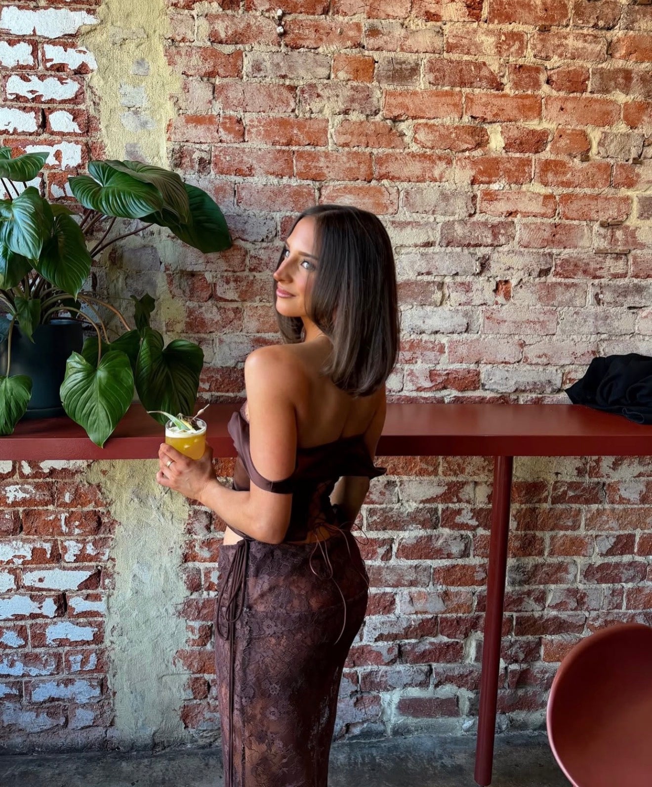 Girl holding a drink and posing. wearing a 2 piece brown lace set.