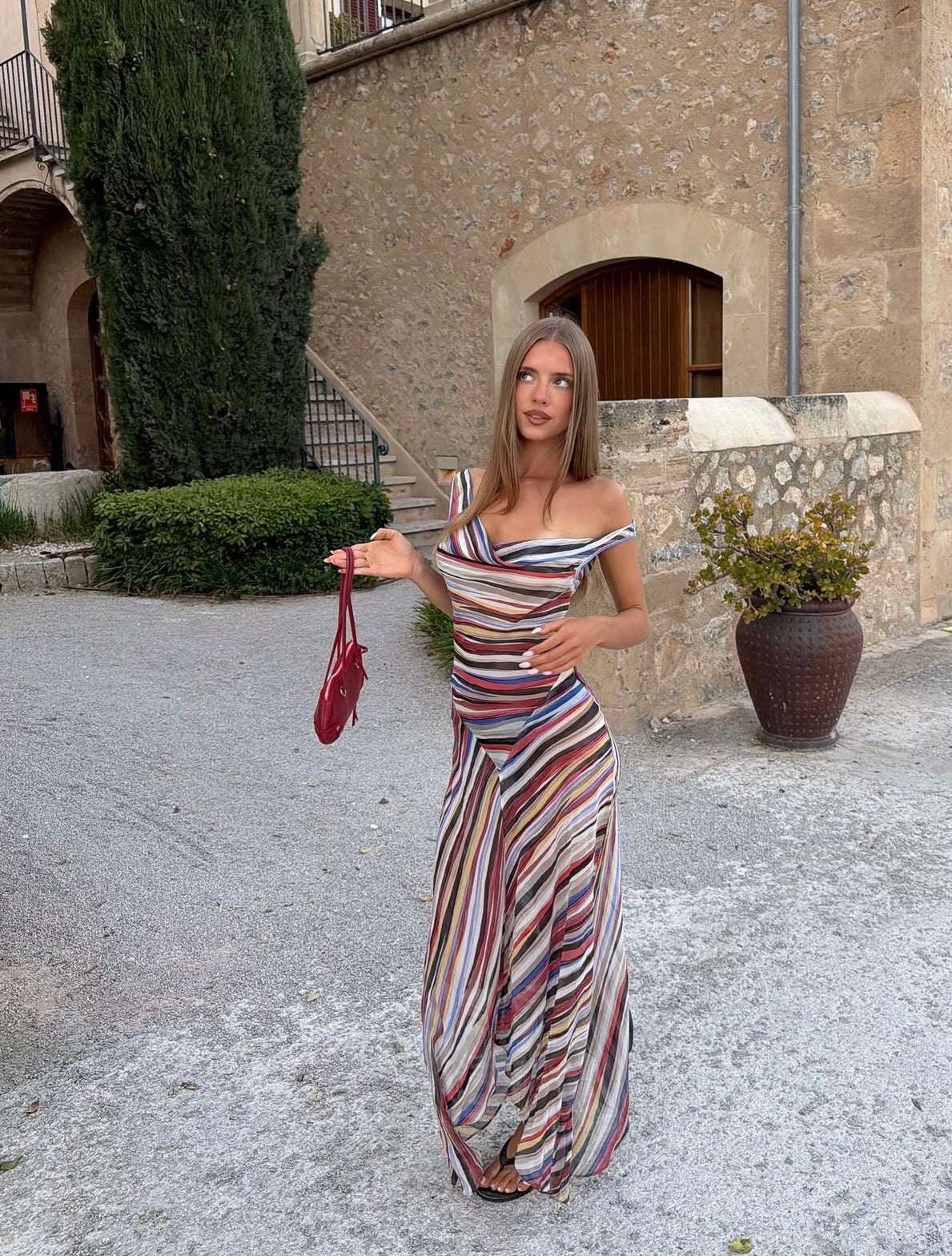 Girl posing with a red handbag on the left hand wearing a striped midi dress.