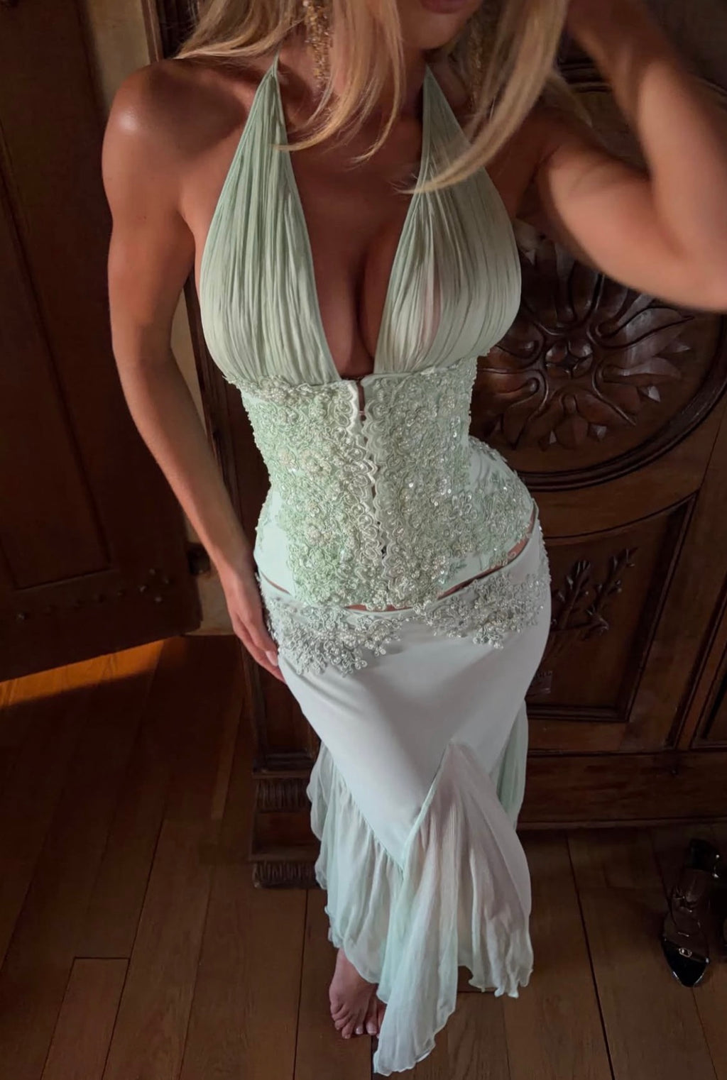 Women wearing a beaded halter green top paired with a sheer skirt standing on wooden floors.