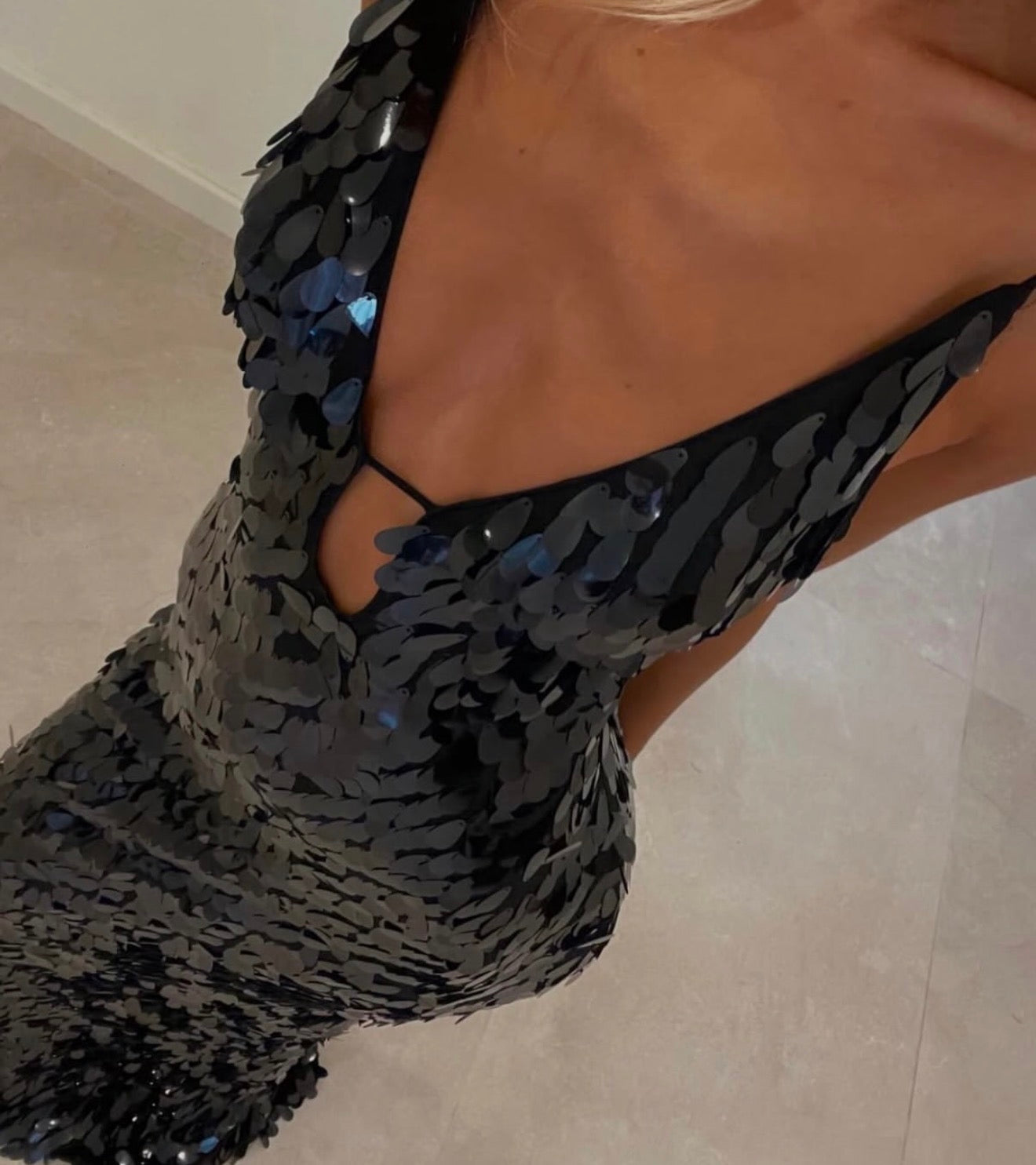 Close-up of a woman wearing a black sequined dress with a deep V-neckline and keyhole cutout detail at the chest.