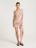Model wearing a pink, cream and brown striped one-shoulder mini dress with draped detailing, long sleeve and tie feature at the hip.