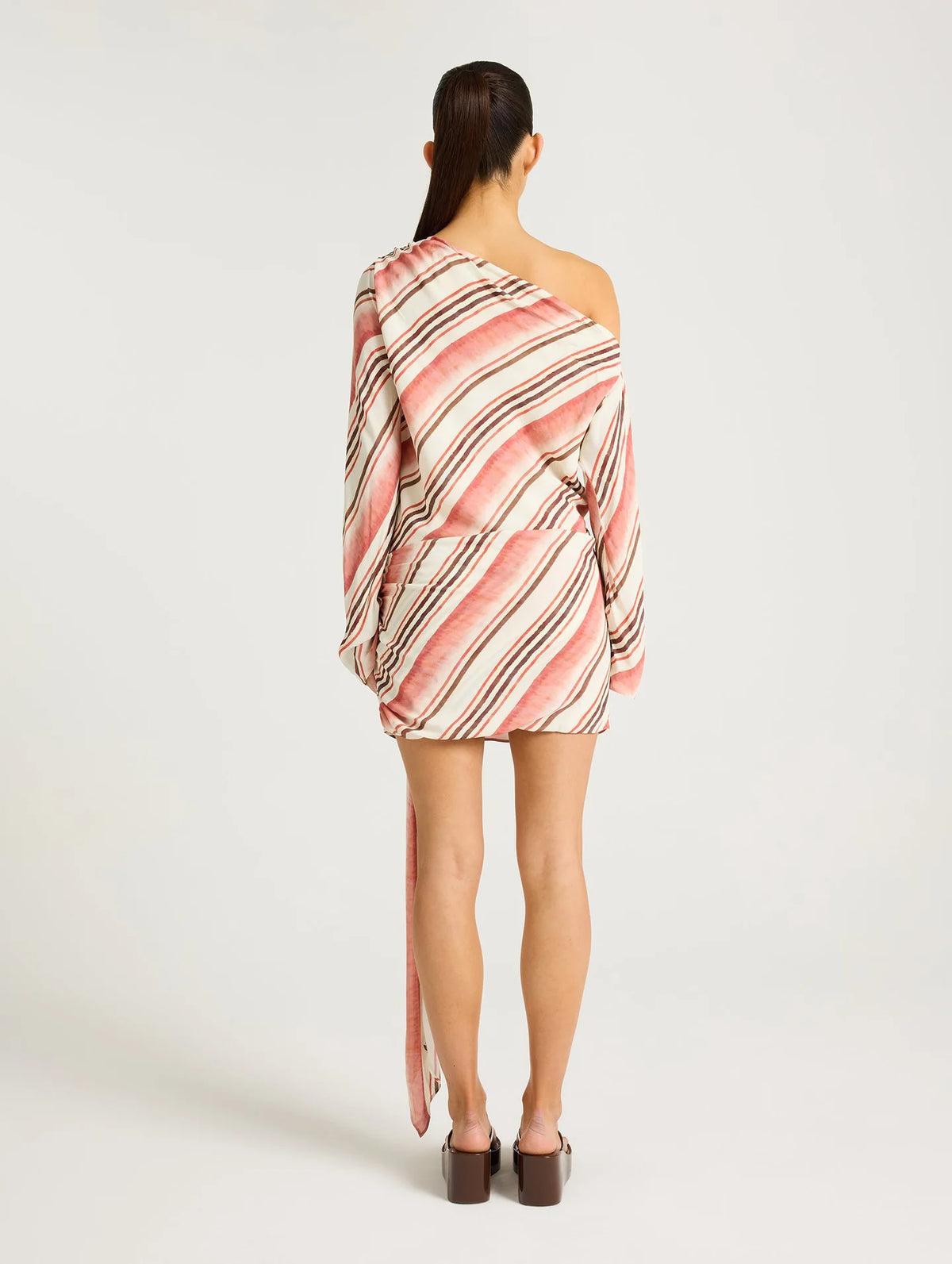Model wearing a pink, cream and brown striped one-shoulder mini dress faced backwards.