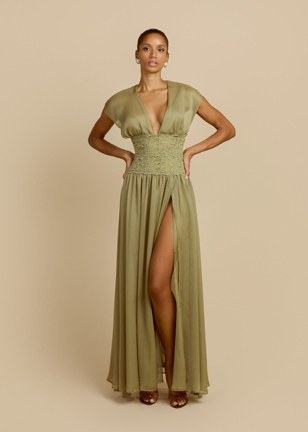 Model wearing a pistachio green floor-length dress featuring a deep V-neckline, soft cap sleeves, fitted lace waist and flowing sheer chiffon skirt.