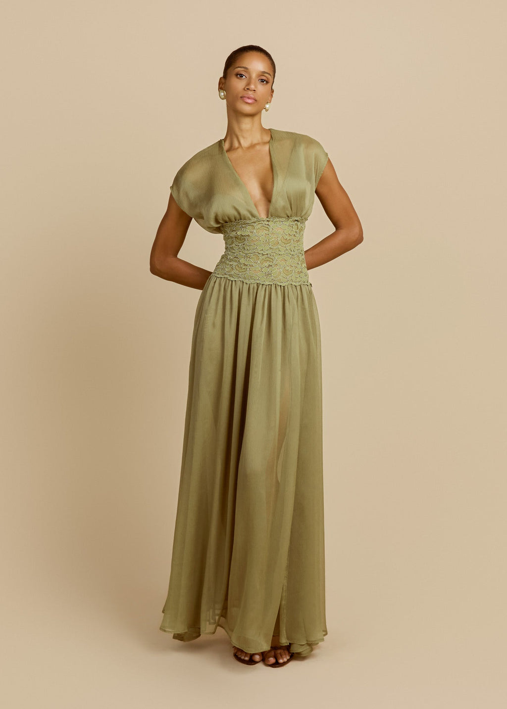 Model wearing a pistachio green floor-length dress featuring a deep V-neckline, soft cap sleeves, fitted lace waist and flowing sheer chiffon skirt.