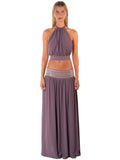 A woman modeling a two-piece halter maxi set in a dusty mauve-purple color. The set features a sleeveless halter crop top and a matching long skirt with a textured metallic silver band at the waist, set against a plain white background.