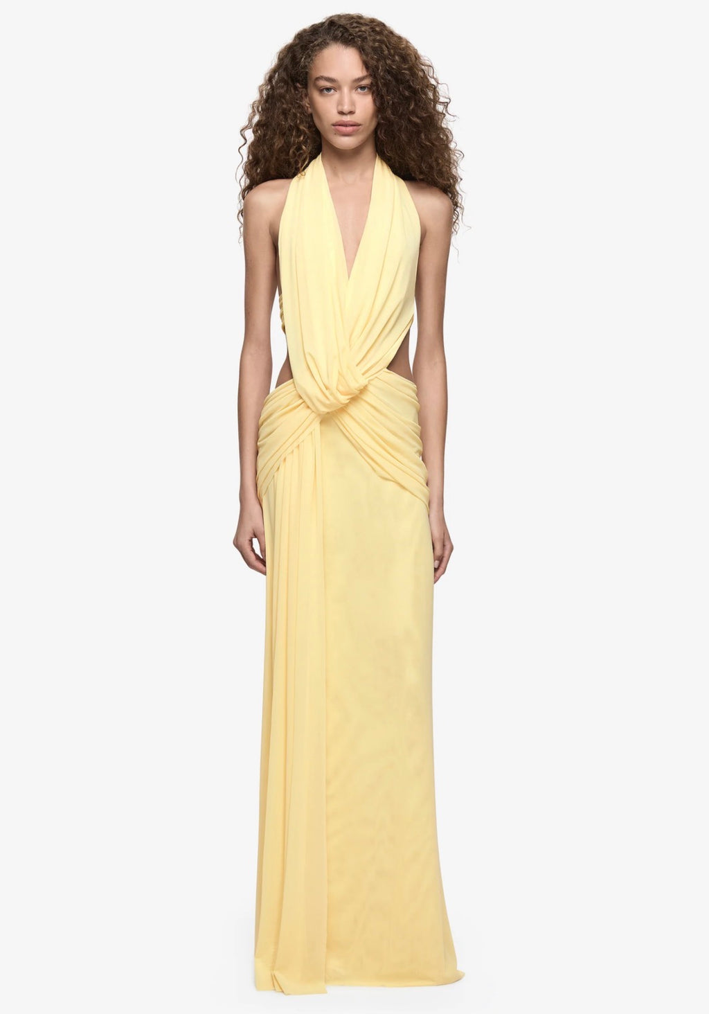  Model wearing a pale yellow halter neck maxi dress with a plunging neckline, draped waist detailing and floor-length silhouette.
