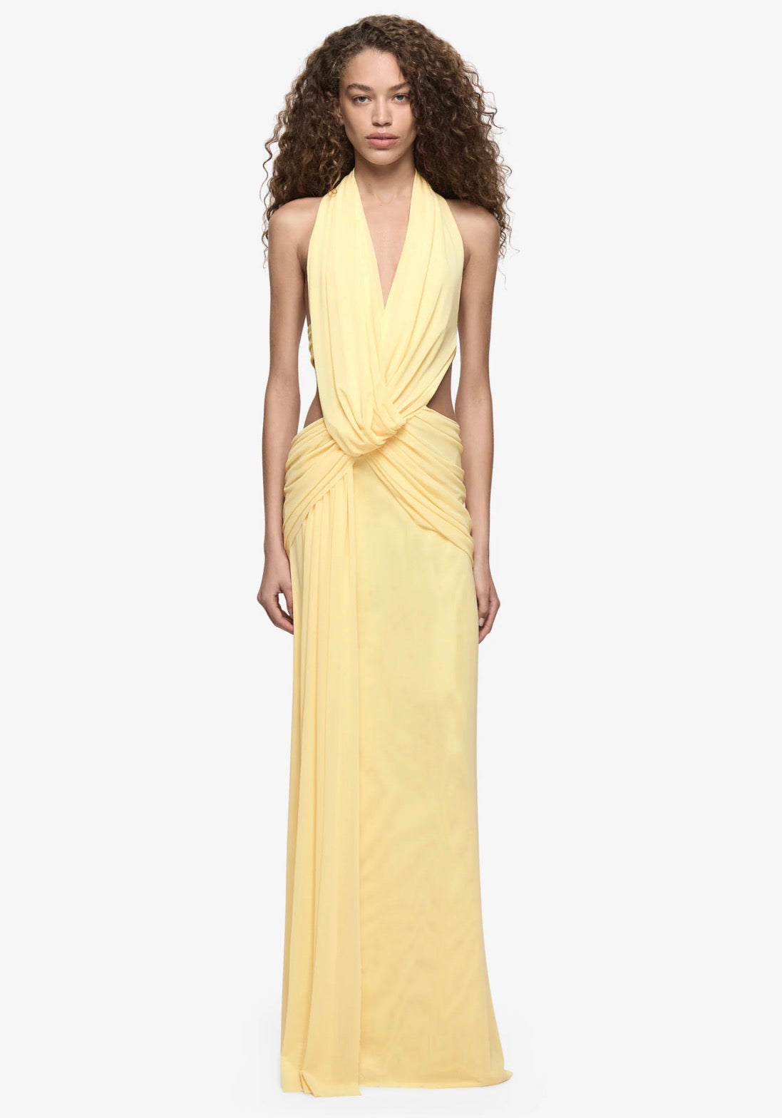  Model wearing a pale yellow halter neck maxi dress with a plunging neckline, draped waist detailing and floor-length silhouette.
