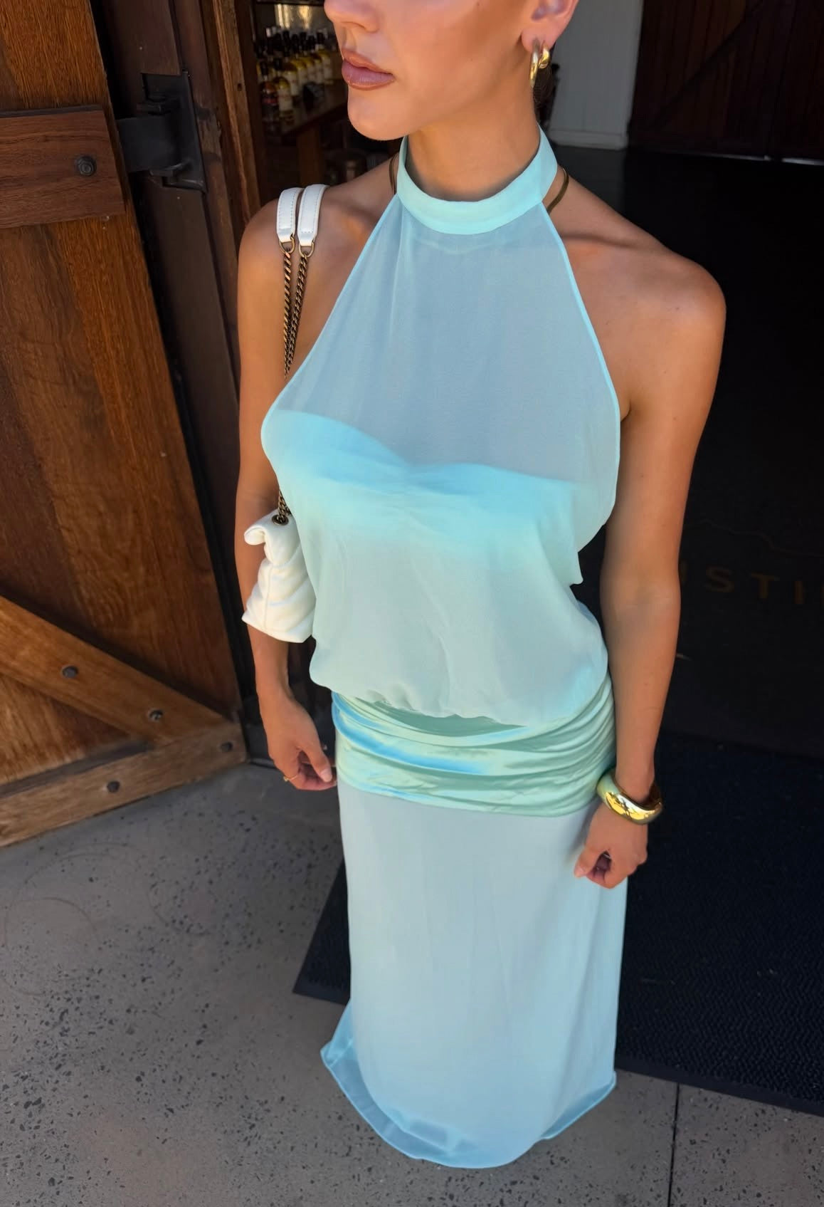 Model wearing a light aqua blue halter neck maxi dress with a sheer bodice, high neckline and ruched waist detailing.